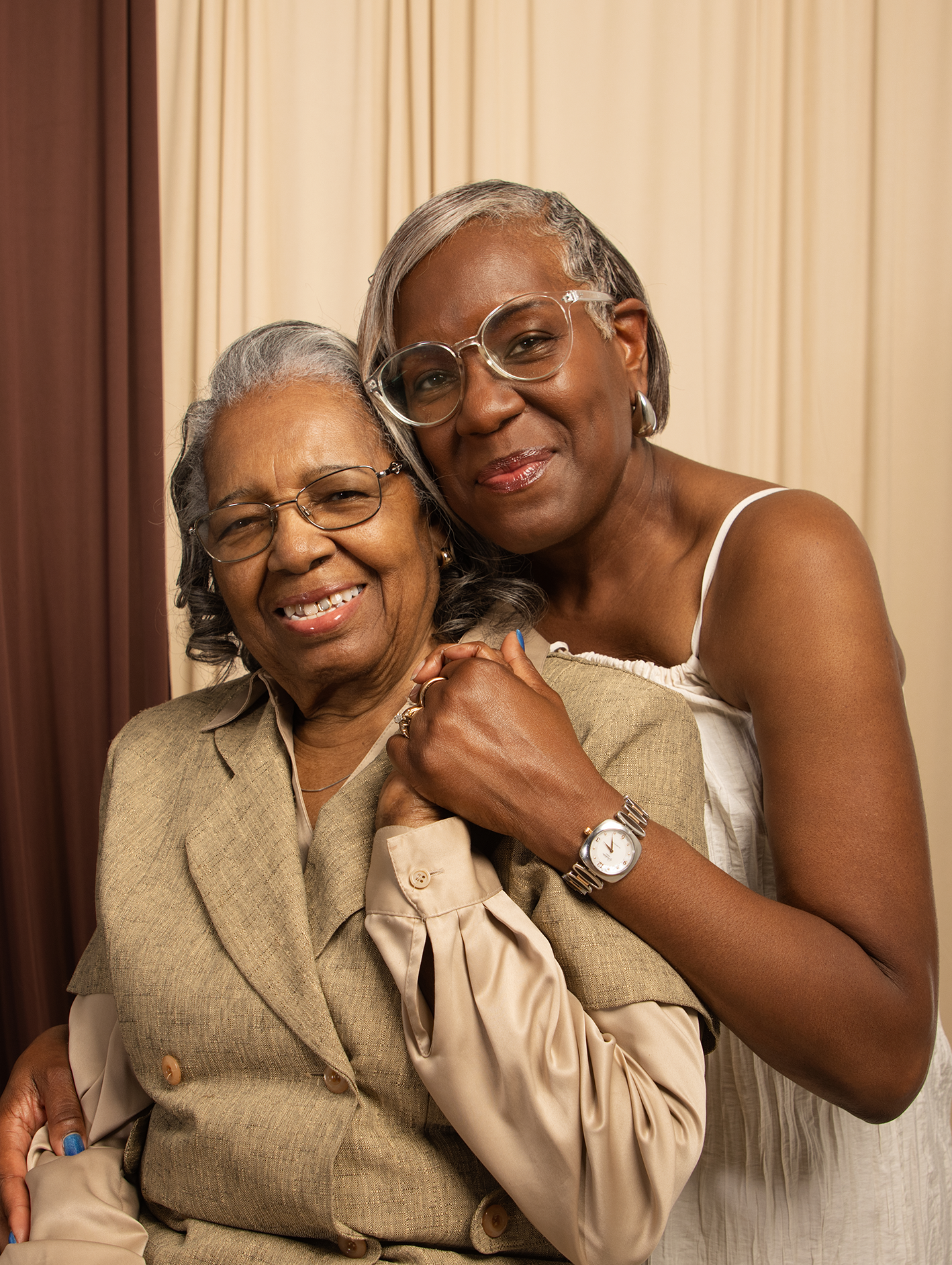 Elderly Black woman and middle-aged woman embracing and smiling in warm studio setting.