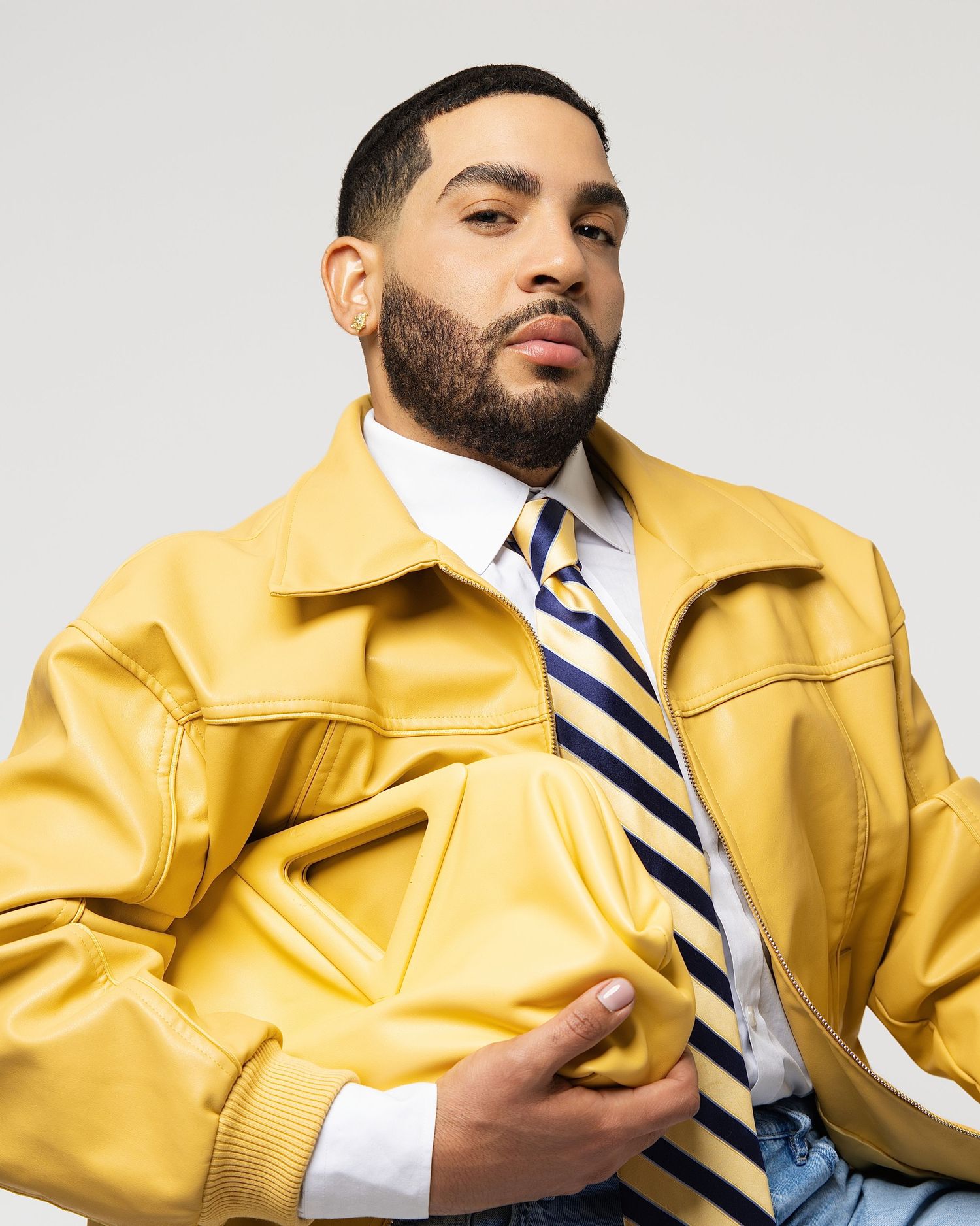Close-up of man in yellow leather jacket and blue striped tie posing against light gray background.