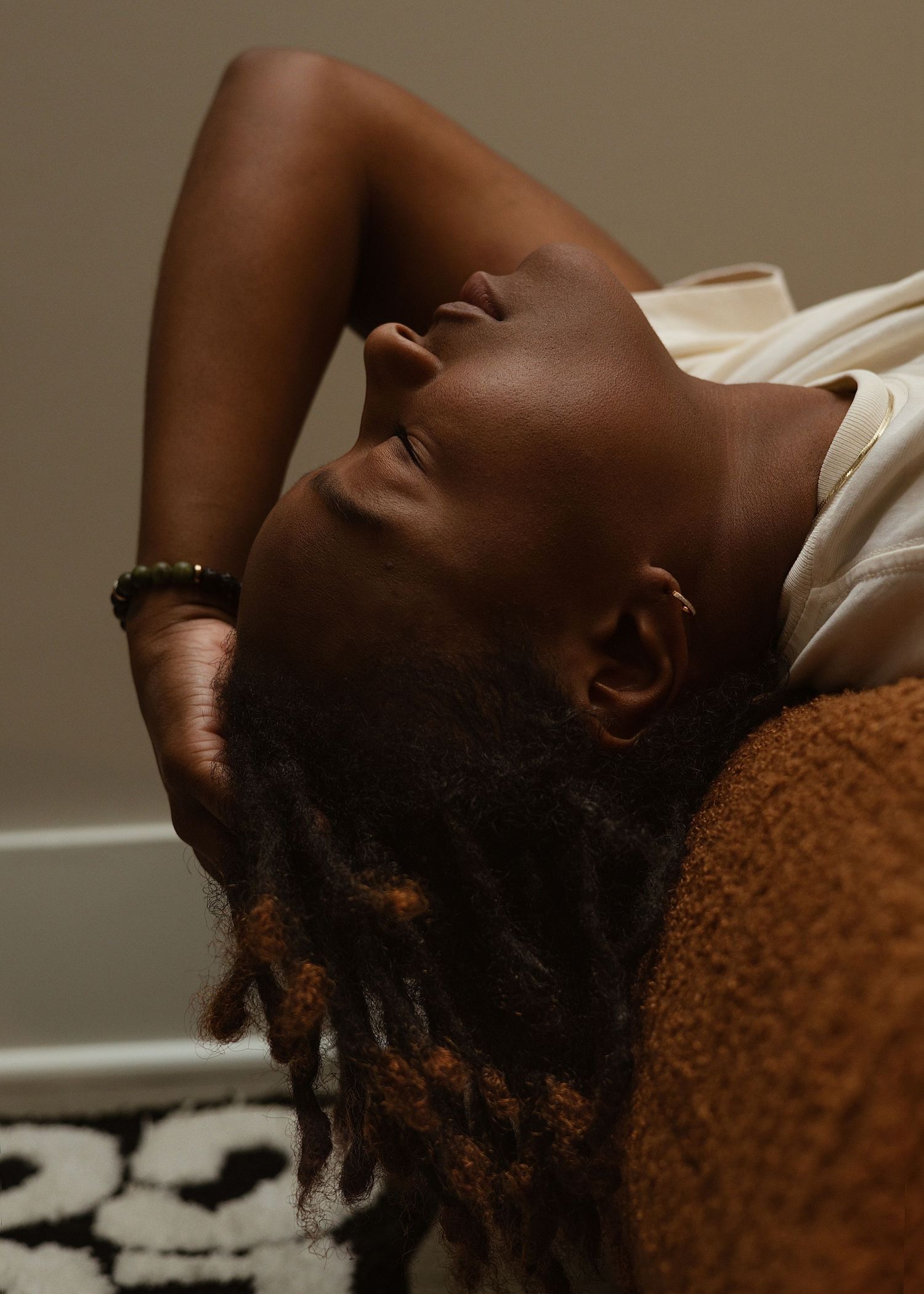 Person with locs reclining peacefully with eyes closed in soft natural light.