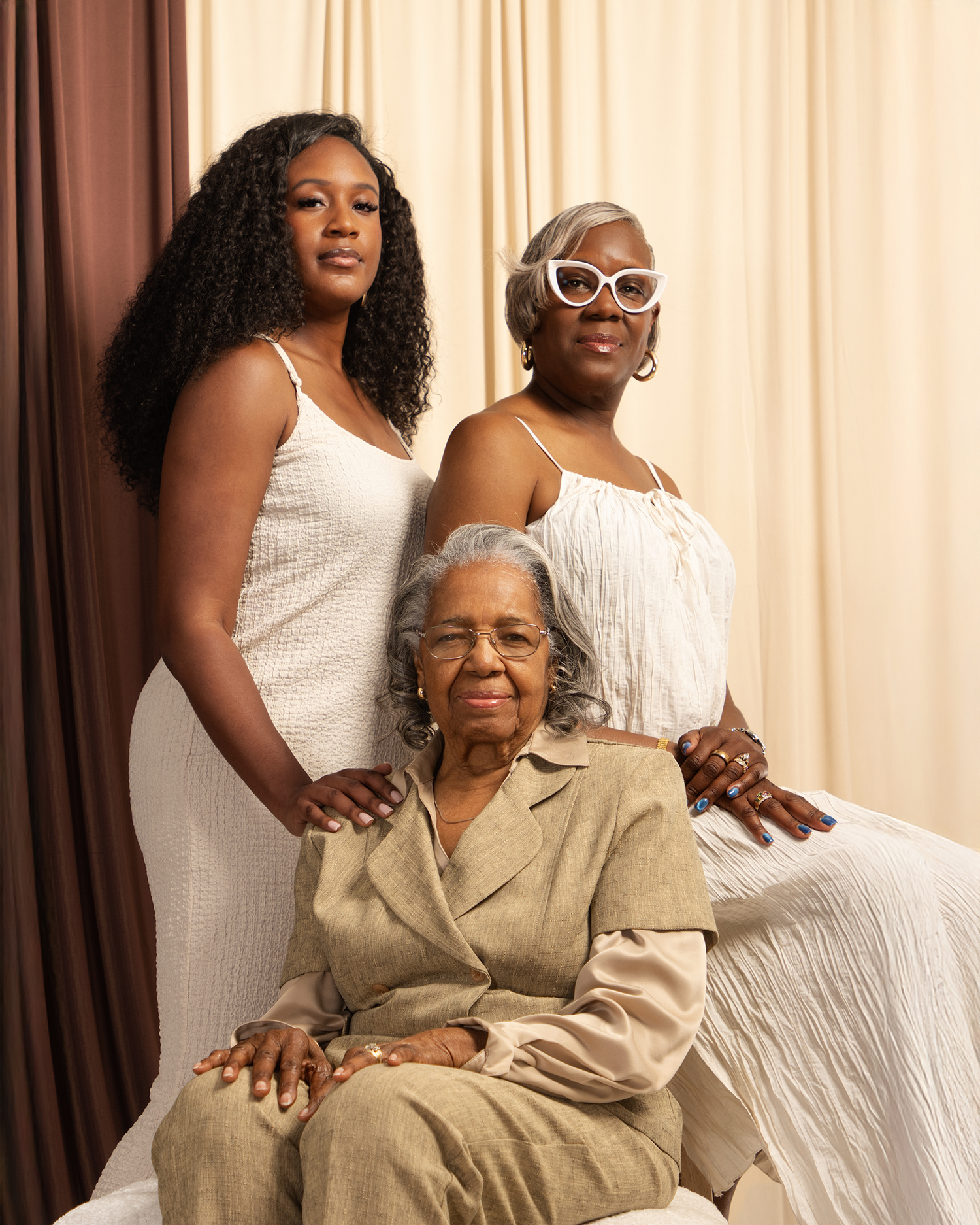 Three generations of Black women pose together in white outfits for an elegant family portrait.