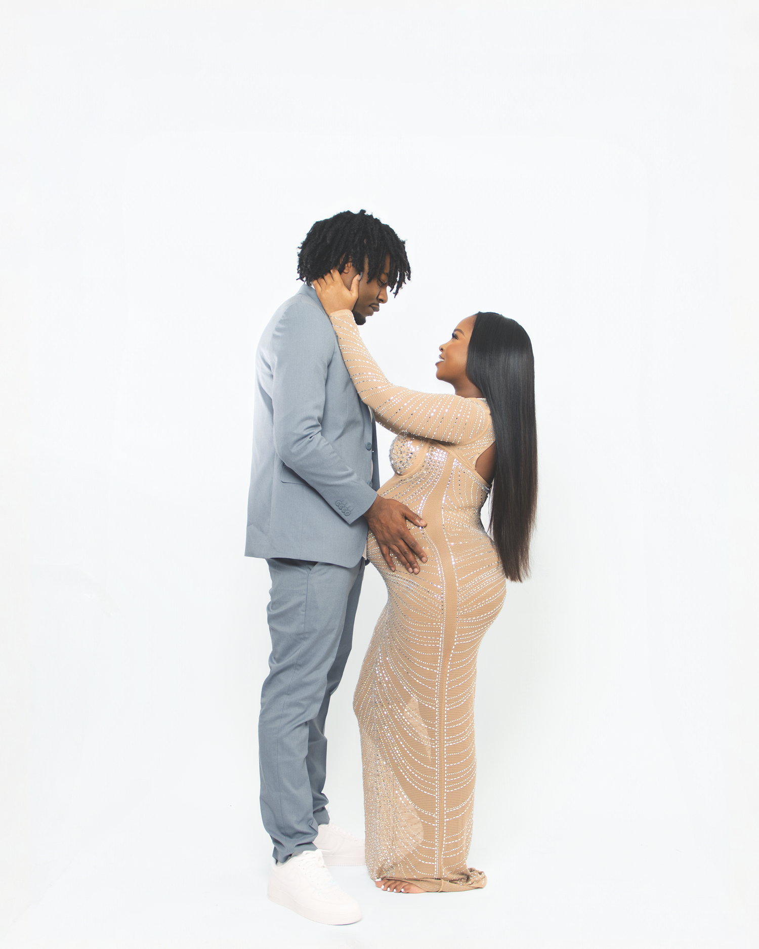 Couple sharing a tender moment in maternity photoshoot, woman in elegant beige dress.