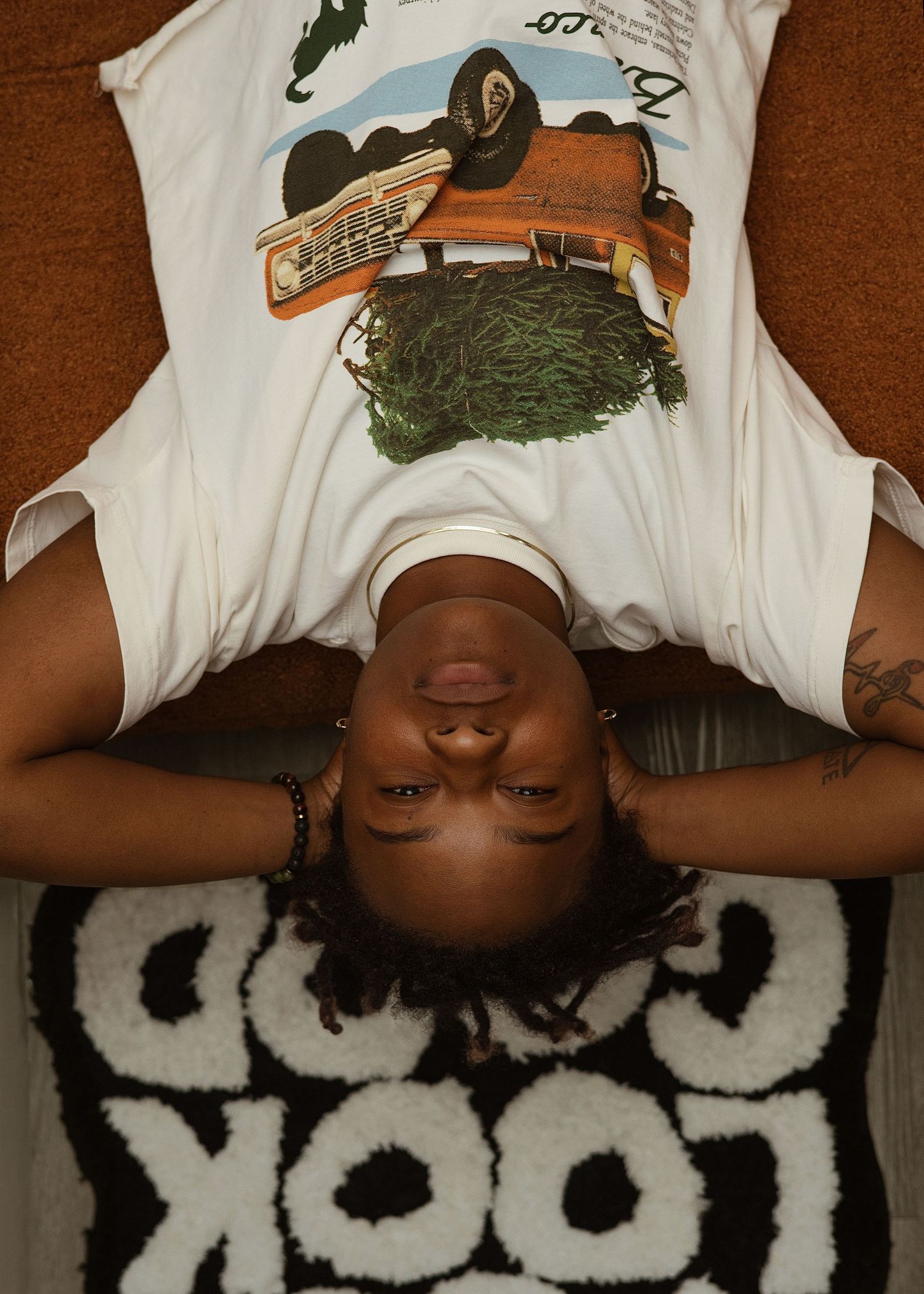 Person with locs lying upside down on carpet near black and white rug.