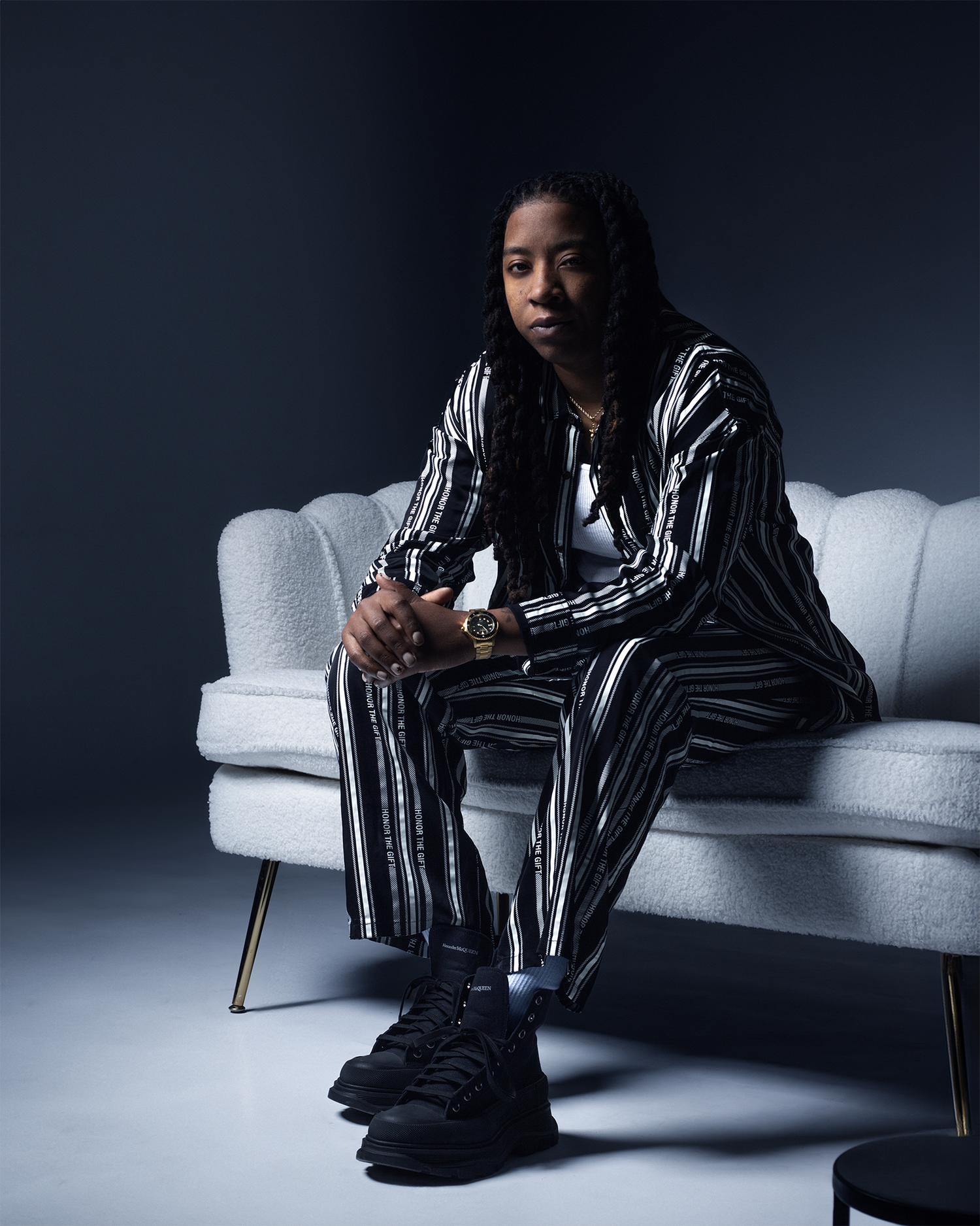 Man in striped suit sits on white sofa in moody studio portrait with dramatic lighting.