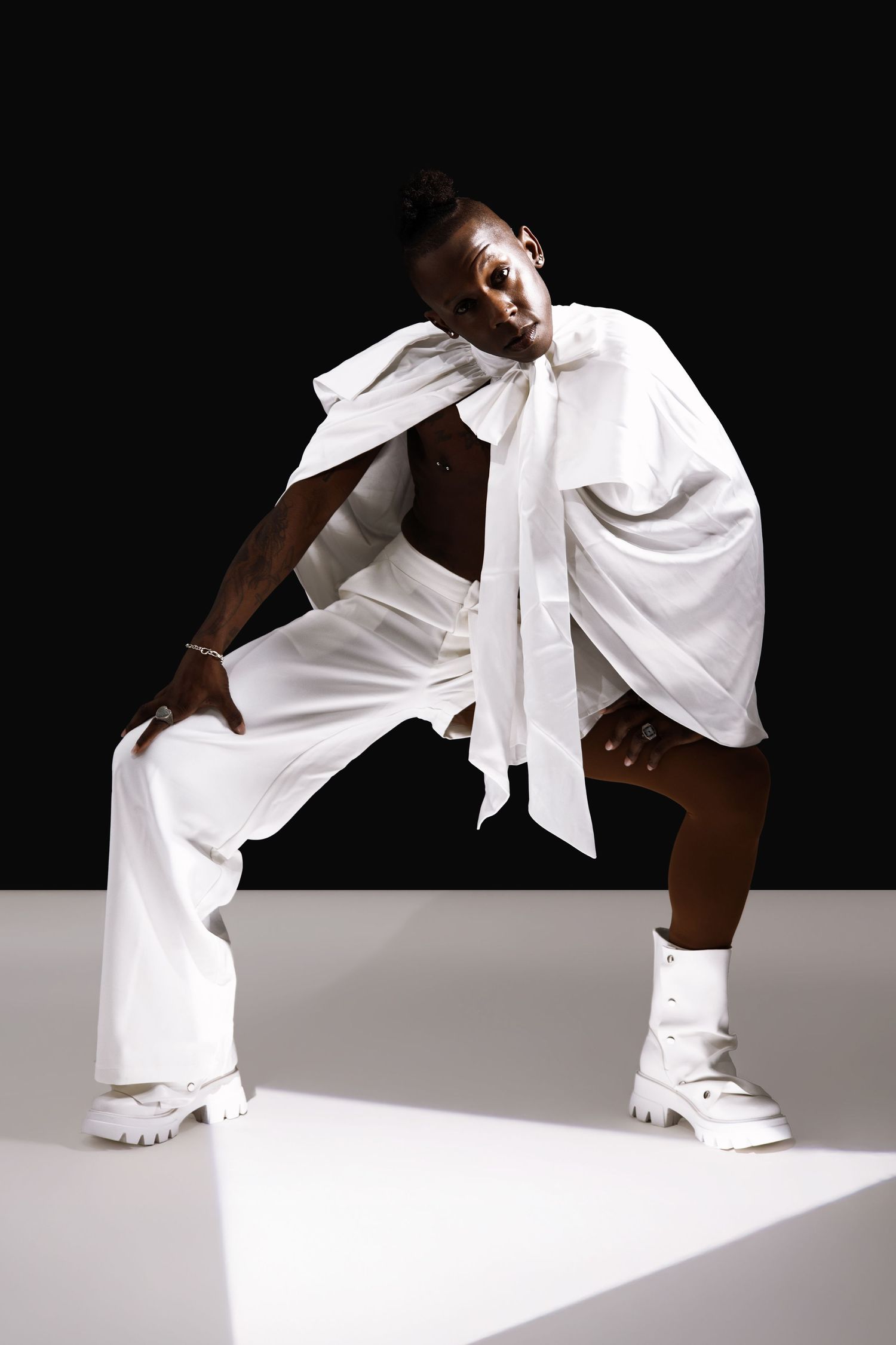Black male model in white wide-leg pants and oversized bow shirt posing in dramatic fashion editorial.