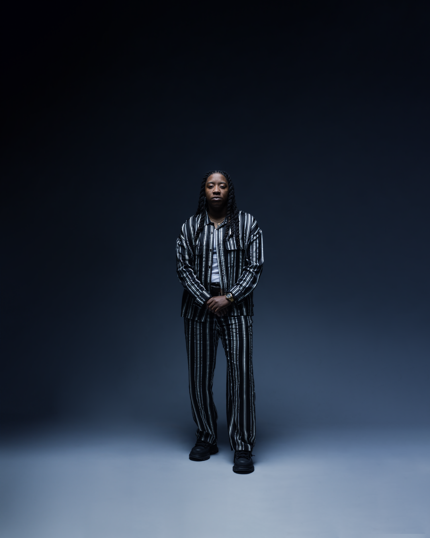 Man in black and white striped suit stands confidently in dramatic studio lighting.