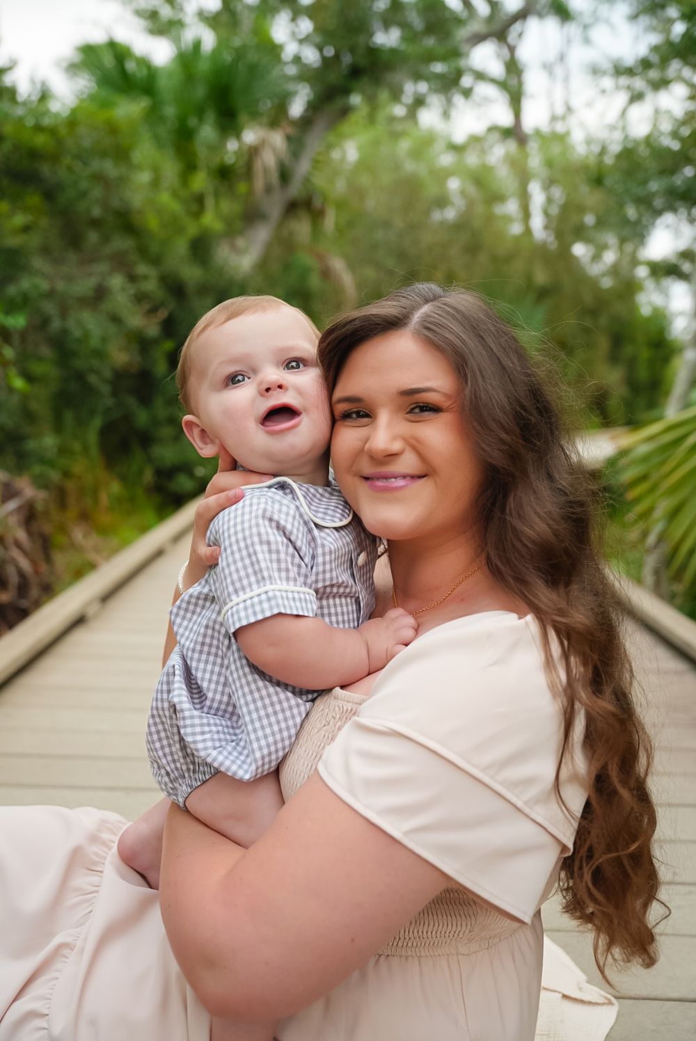 Mom holding her smiling baby boy on a boardwalk by the beach
