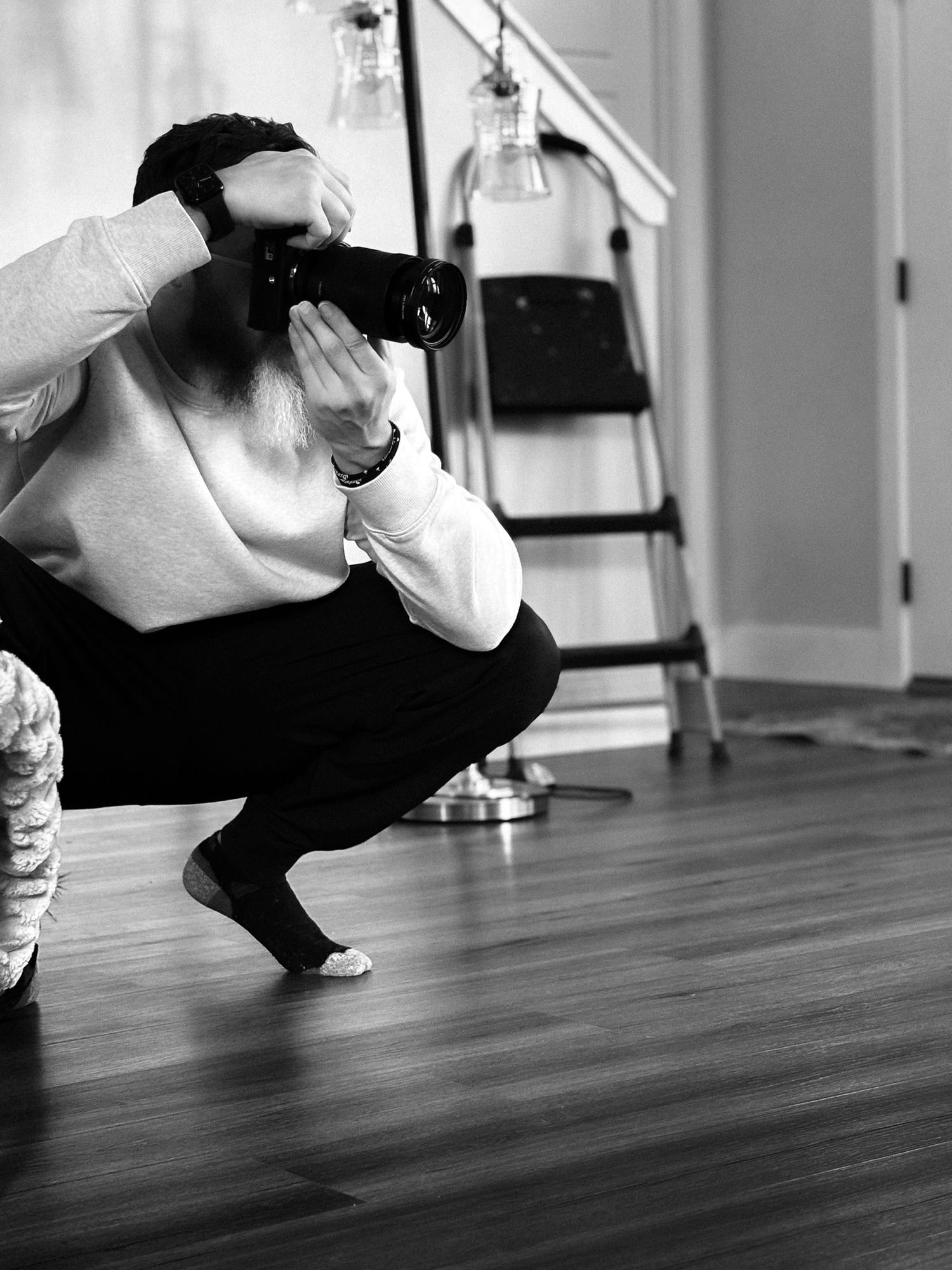 Black and white photo of a photographer crouching low to capture a shot in a bright studio space.