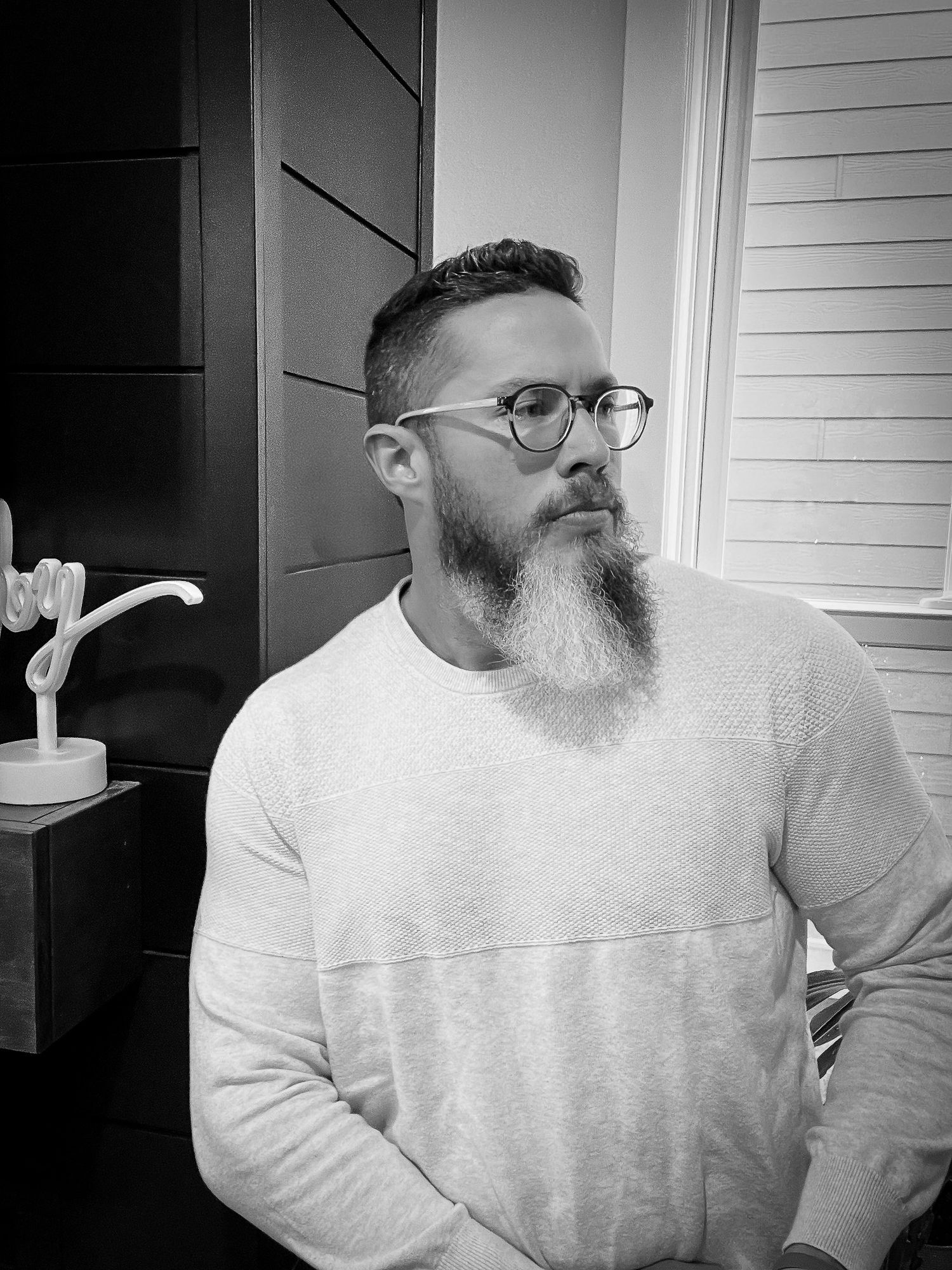Black and white portrait of a bearded man with glasses wearing a light sweater.