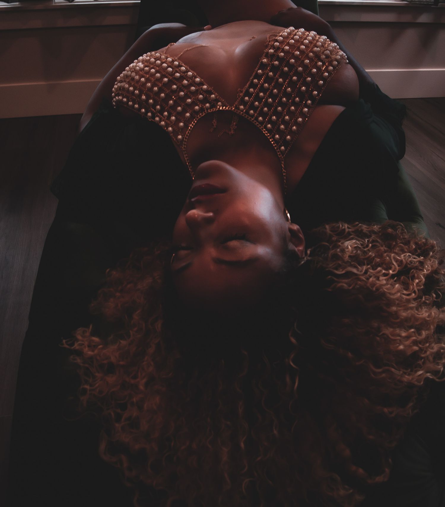 Woman in a pearl-embellished crop top lying on a floor with curly hair spread around her.