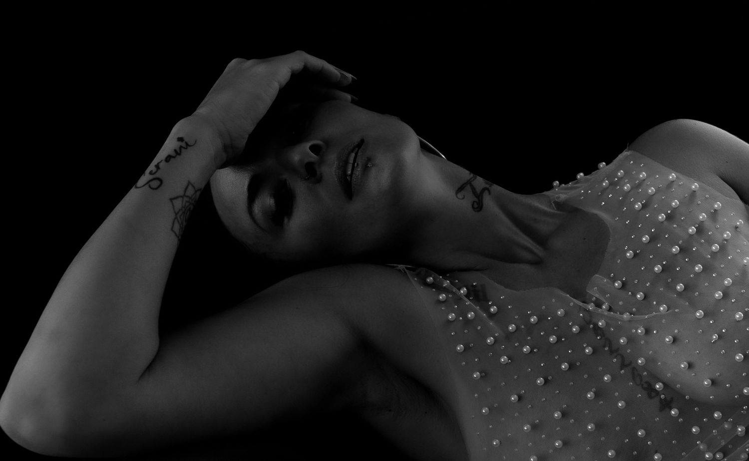Black and white artistic portrait of a woman in a pearl-embellished top lying back dramatically.