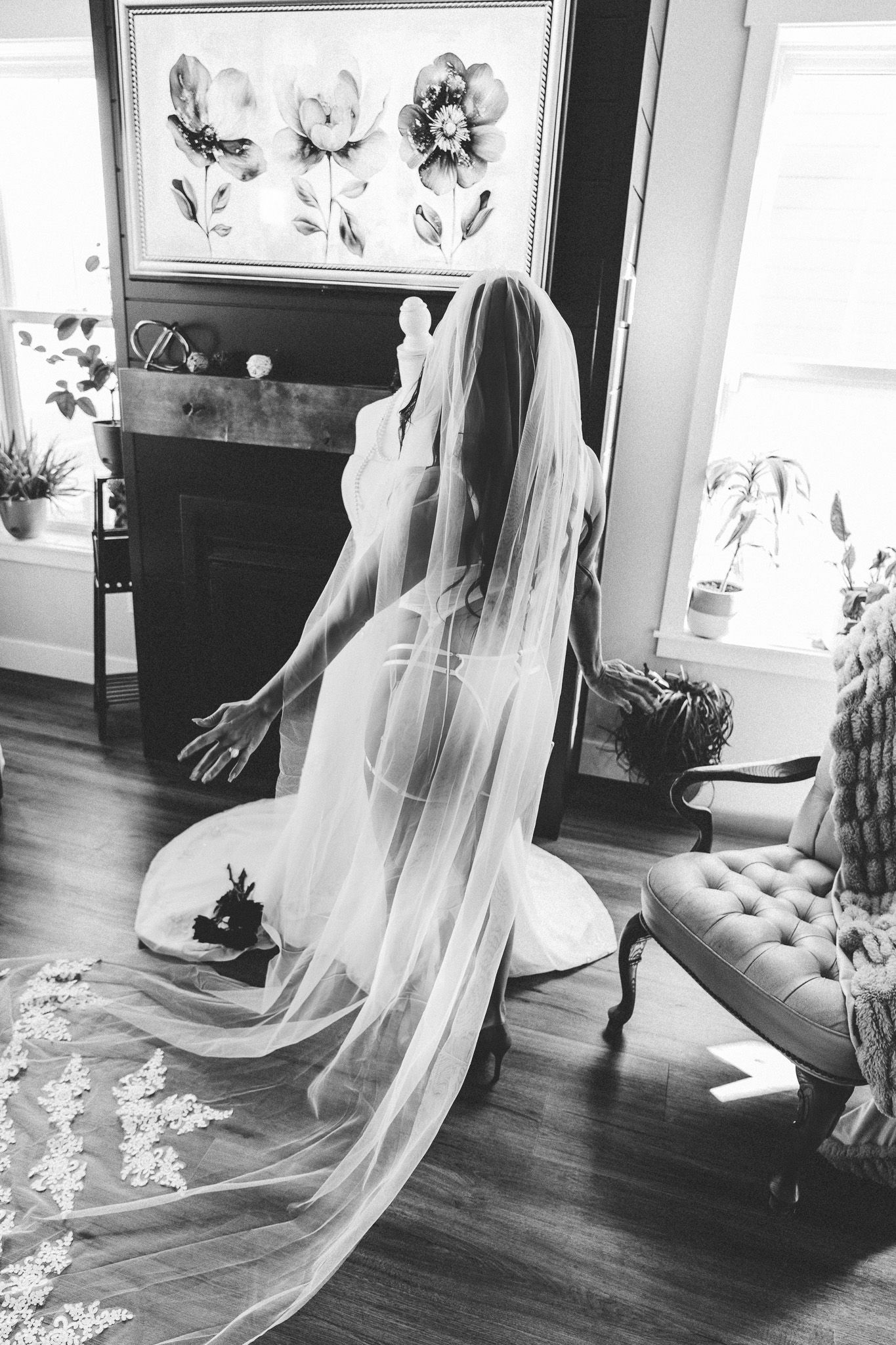 Black and white boudoir photo of bride in sheer veil kneeling on floor near fireplace.