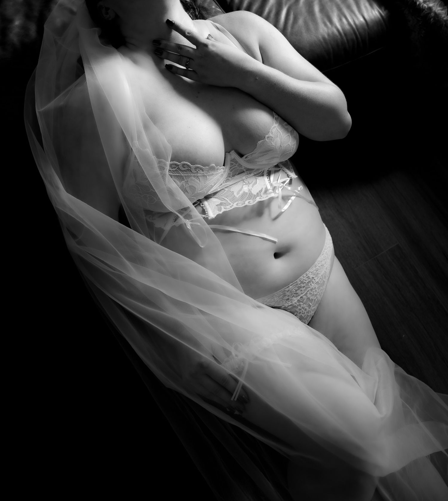 Black and white bridal boudoir photo of woman in white lingerie draped with tulle veil.