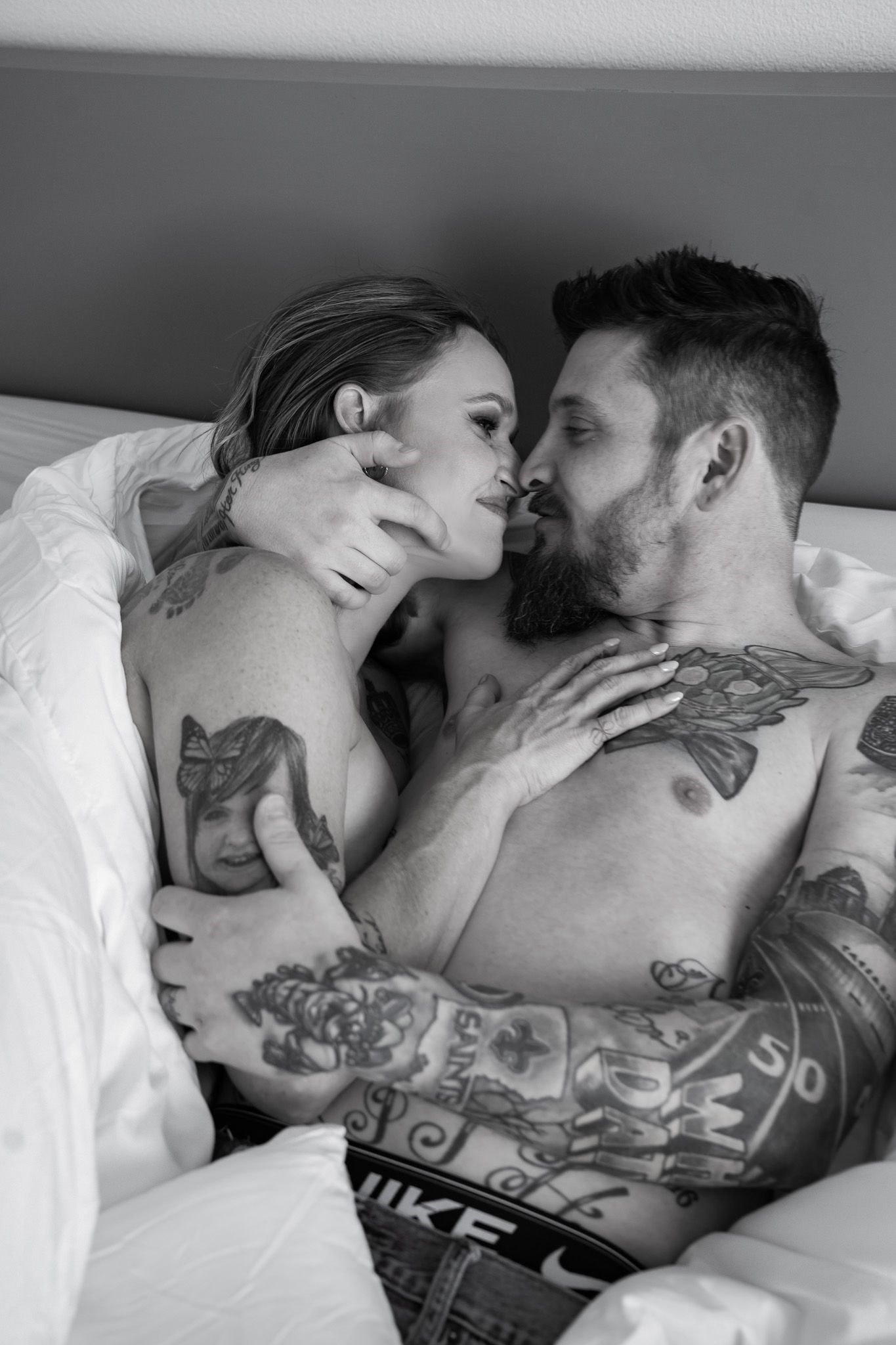 Black and white photo of a tattooed couple kissing passionately in bed.