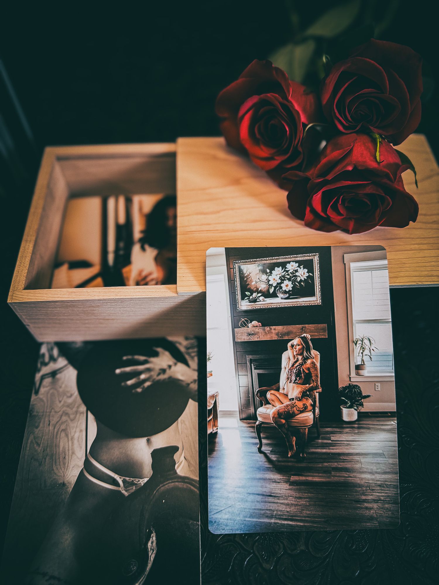 Printed boudoir photos and wooden keepsake box with red roses on a dark surface.