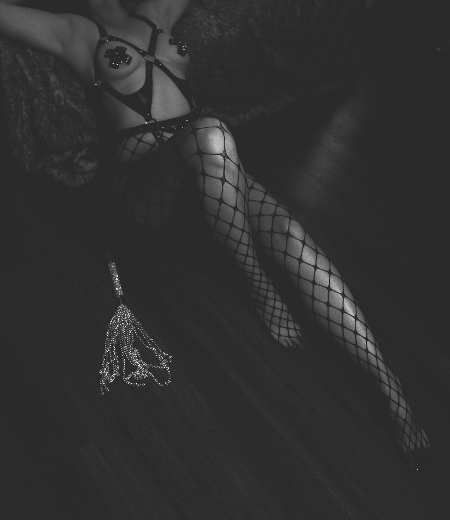 Black and white boudoir photo of a woman in fishnet stockings and lace lingerie lying on a dark floor.