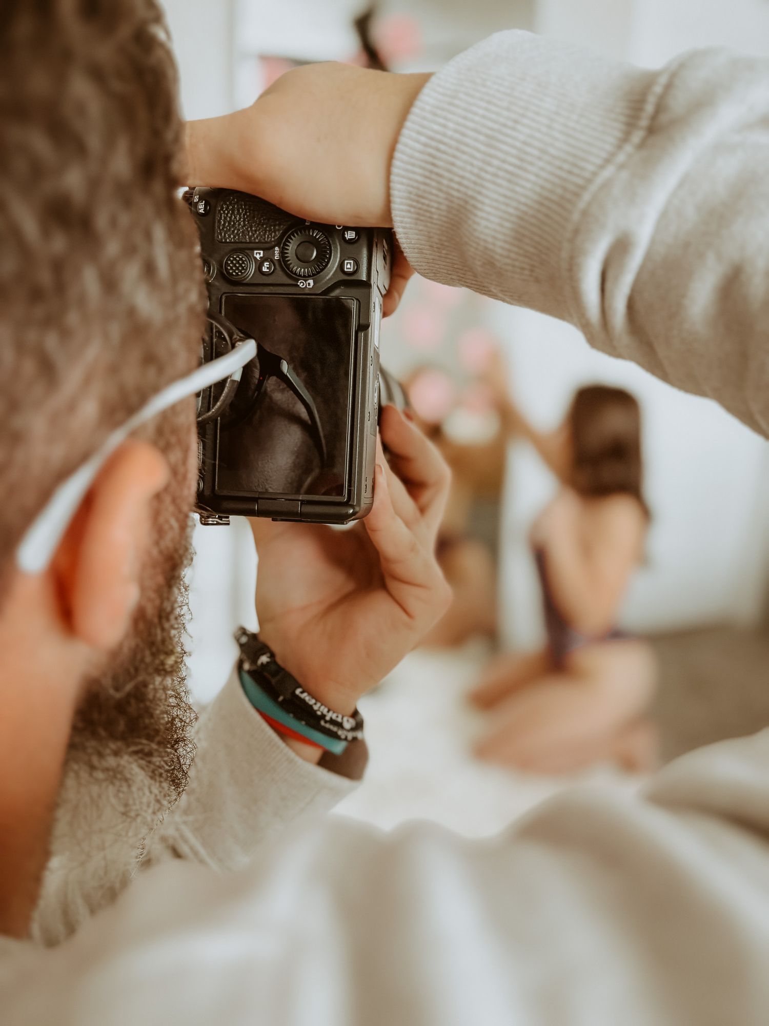 A bearded photographer reviews images on a camera screen during a professional boudoir photography session.