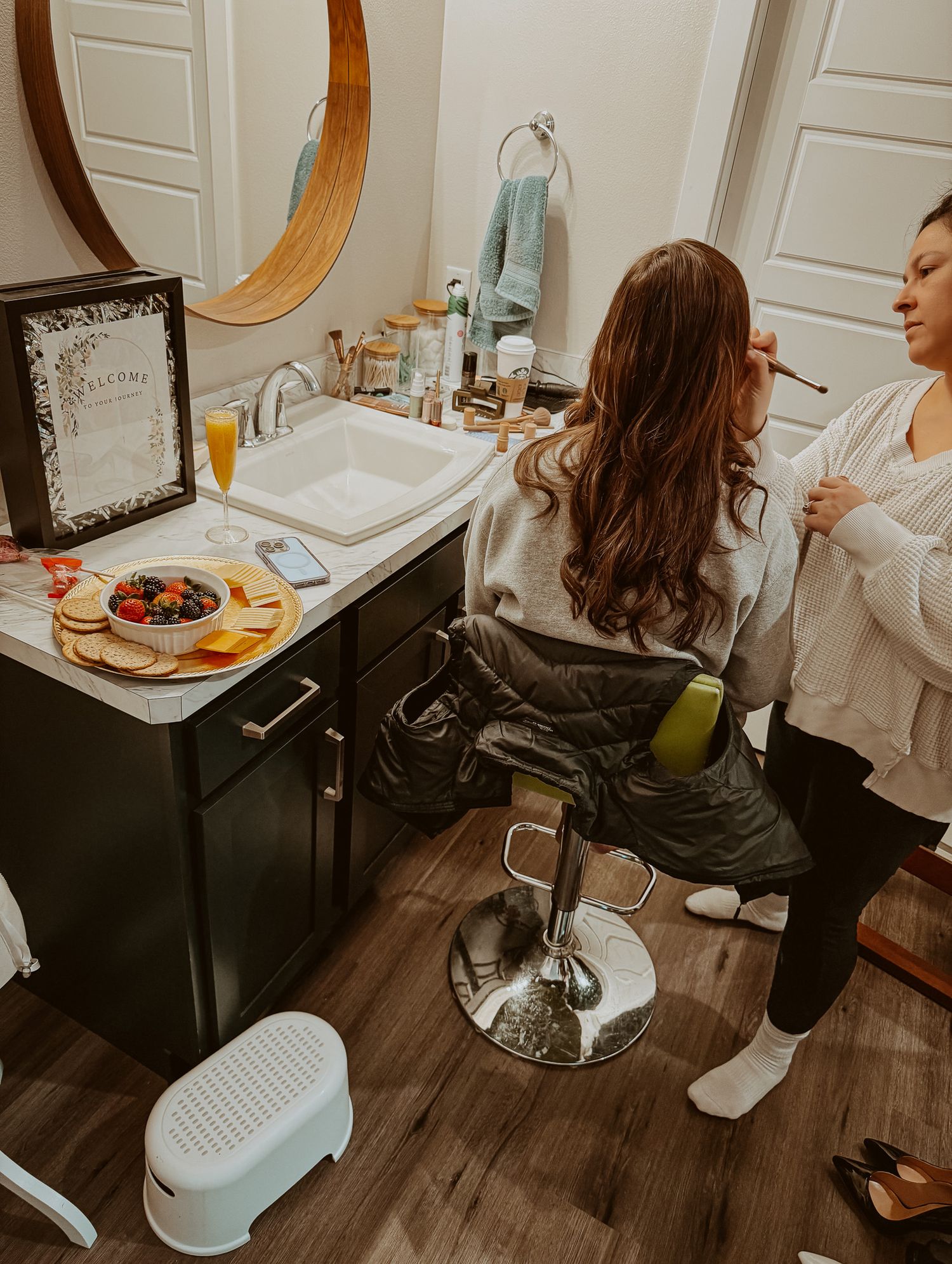 Woman getting makeup done in a salon chair during a bridal preparation session in a stylish bathroom.