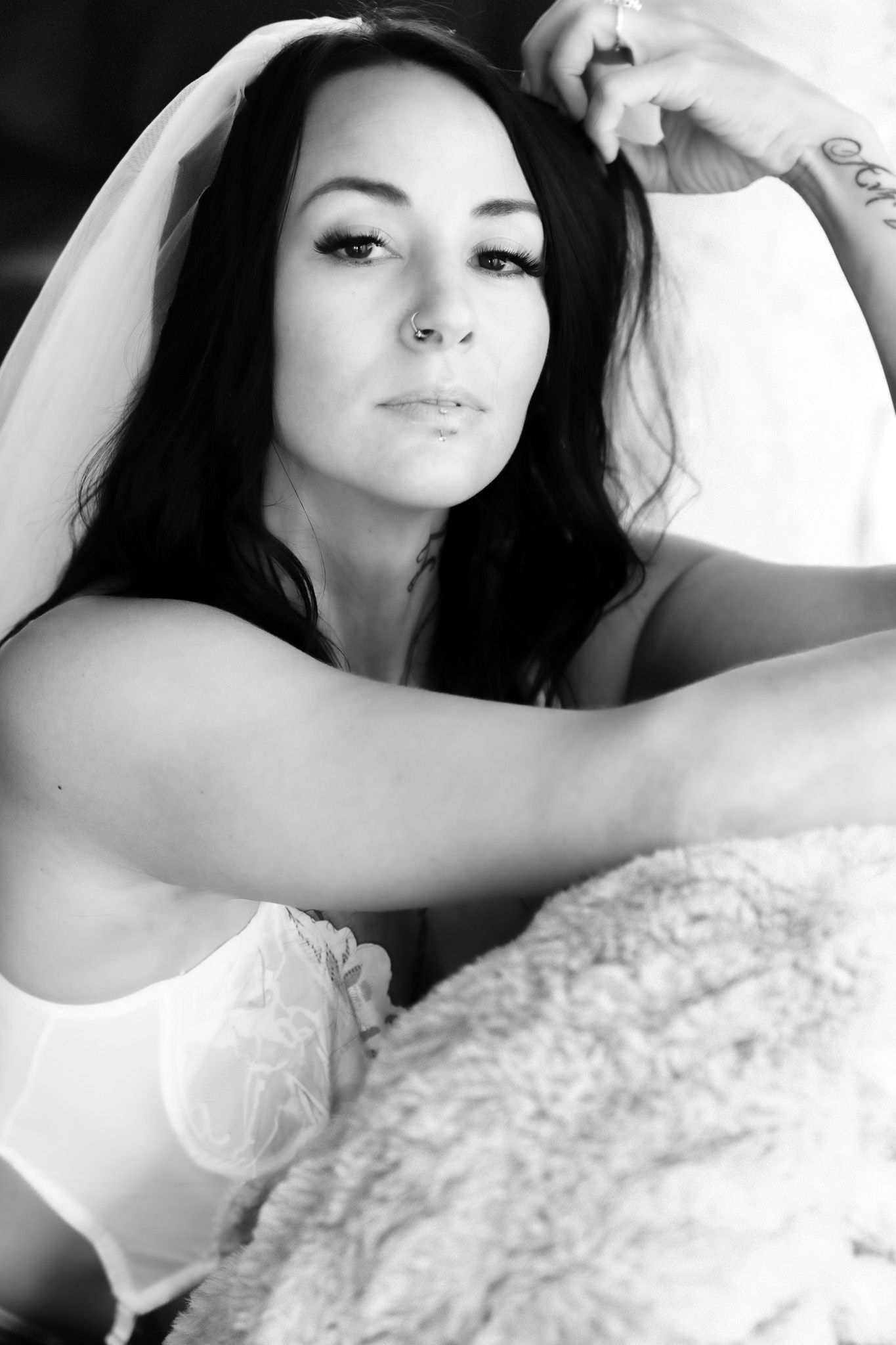Black and white portrait of dark-haired woman in white bra and bridal veil on fur blanket.