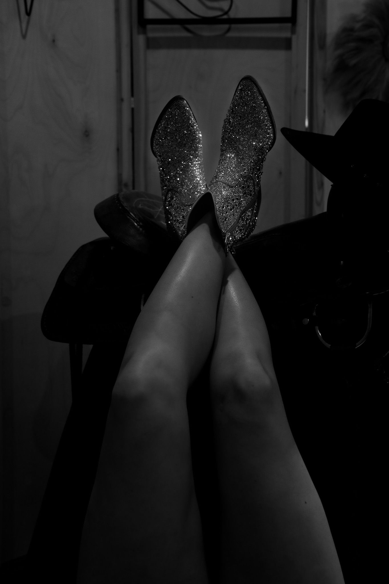 Black and white photo of crossed legs wearing sparkling glitter ankle boots elevated in the air.