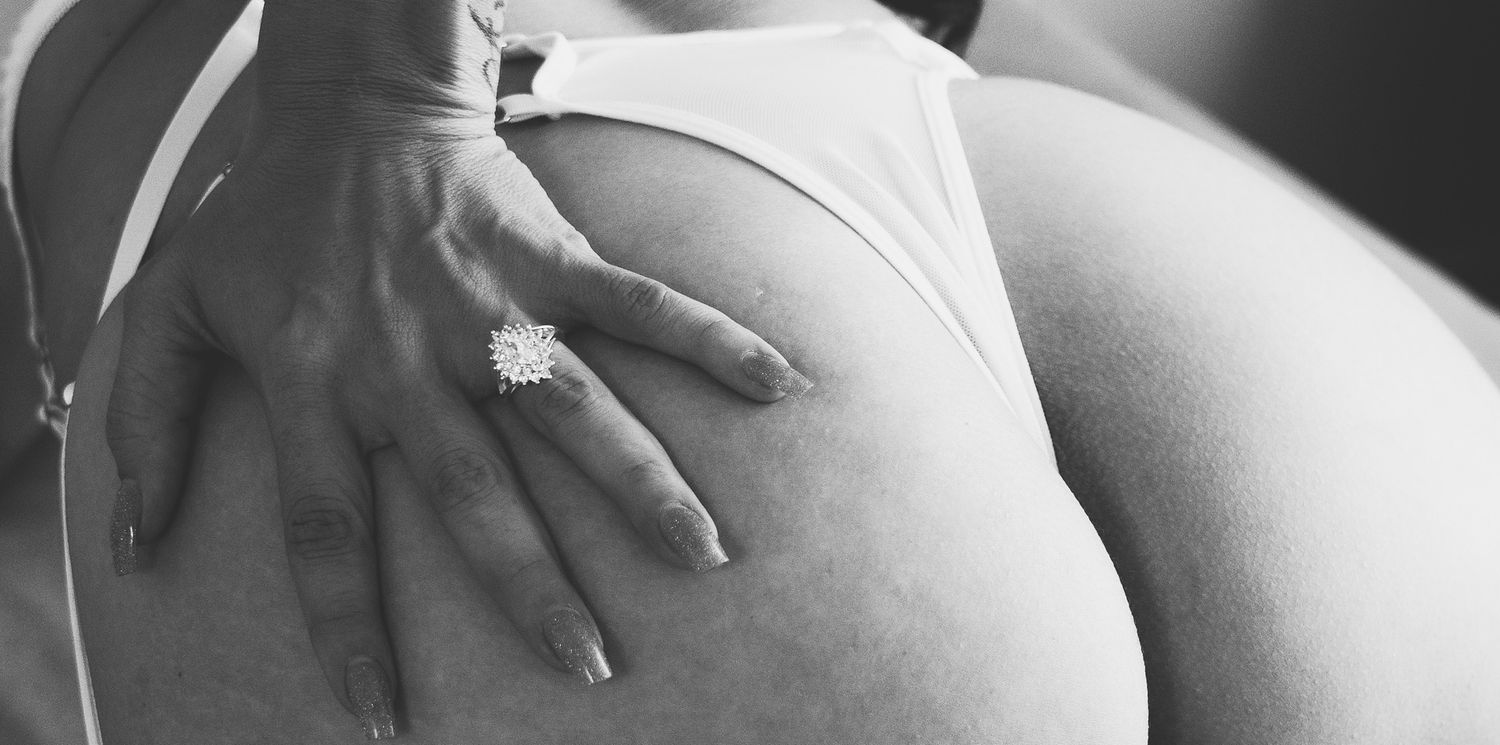 Close-up black and white boudoir photo of woman in white lingerie with diamond engagement ring.