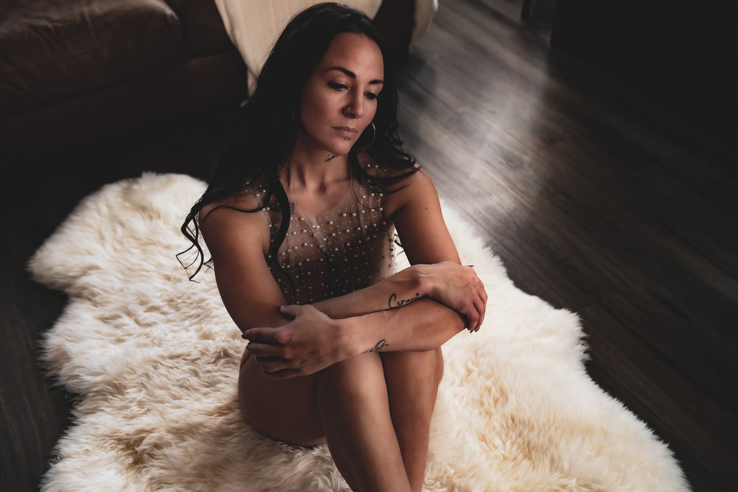 Woman in beaded dress sitting on white fur rug on dark hardwood floor.