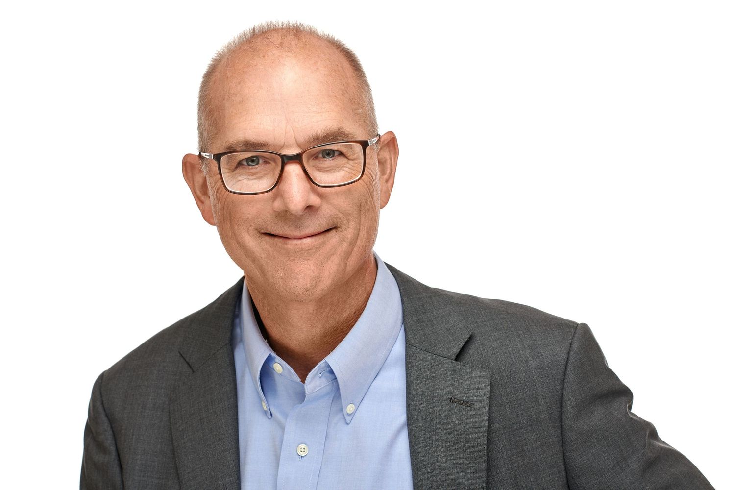 Professional headshot of a bespectacled older man in a gray suit and light blue shirt smiling warmly.