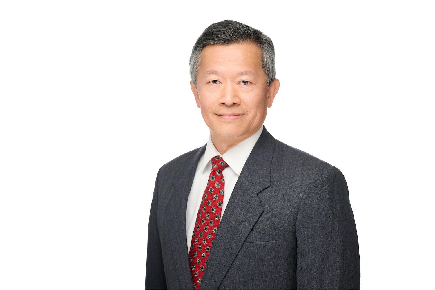Professional Asian businessman in gray suit and red tie poses confidently against white background.