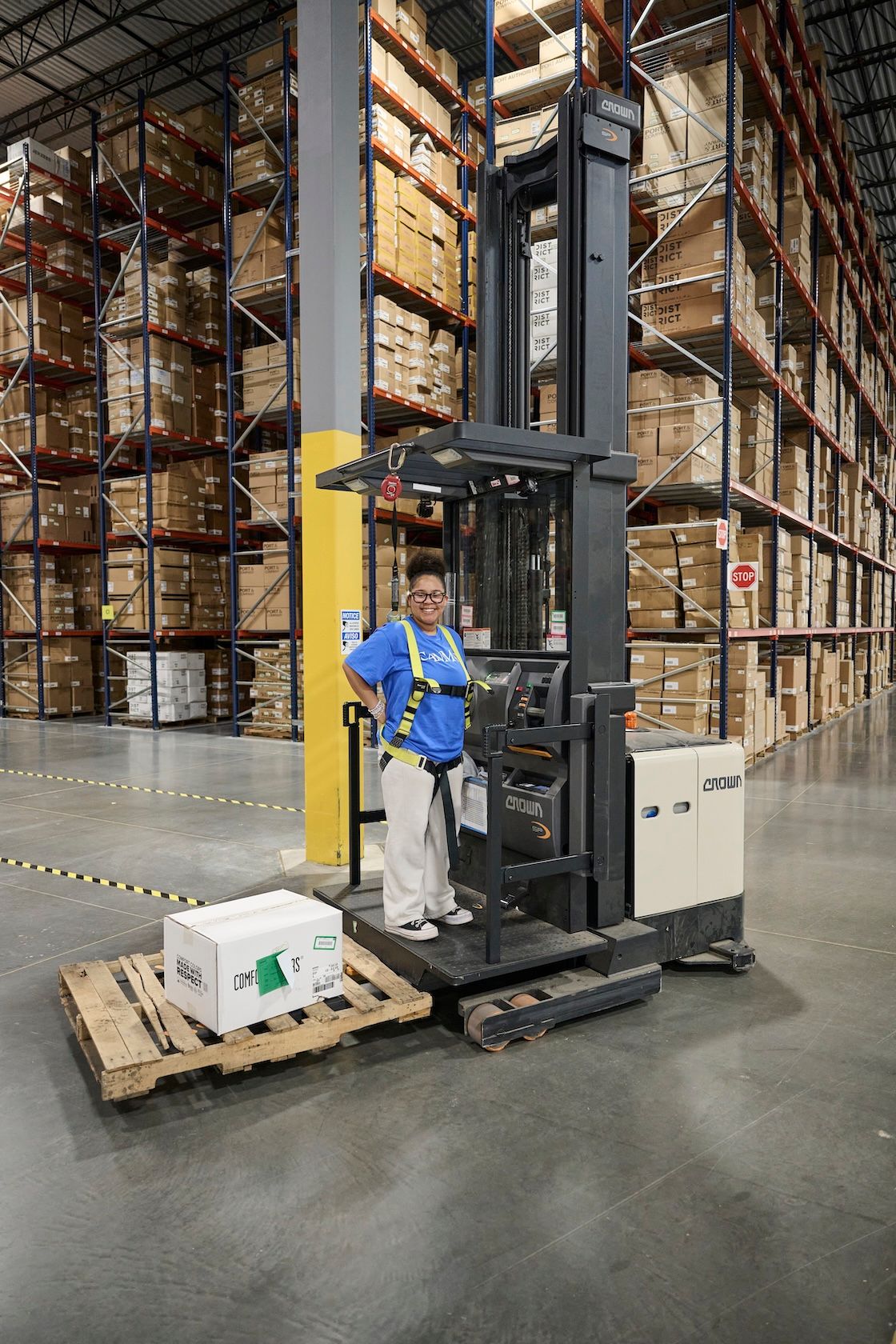 Warehouse worker in blue shirt operating Crown forklift in large distribution center.