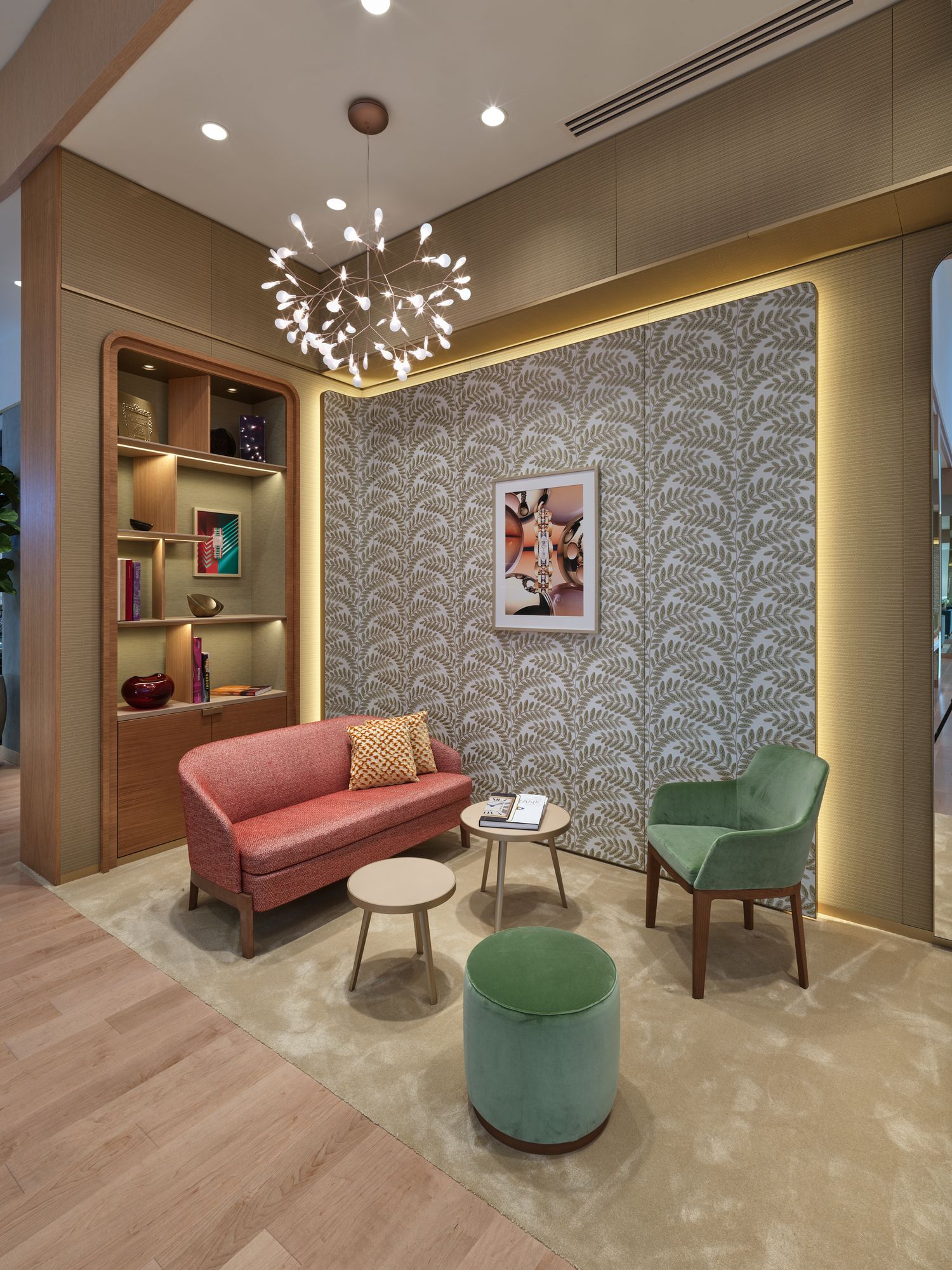 Elegant hotel lounge seating area with pink sofa, green chair, patterned wallpaper, and chandelier.