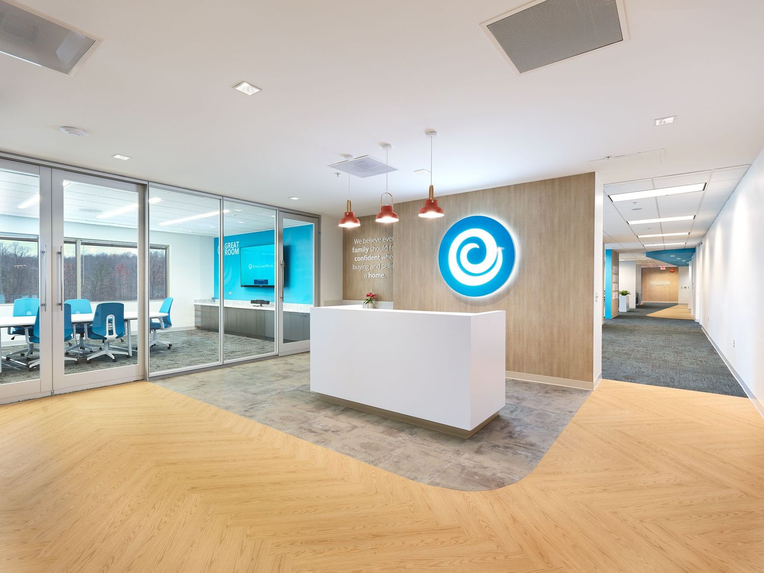 Modern office reception area with white desk, herringbone wood floors, and blue spiral logo on wall.