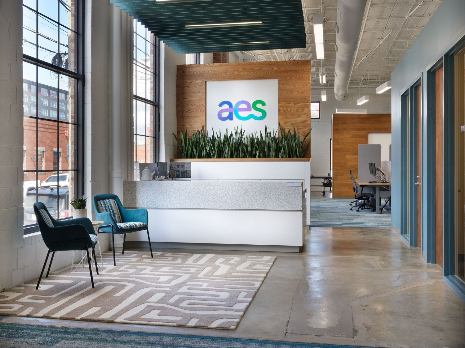Modern AES corporate office reception area with logo wall, teal chairs, and open workspace.