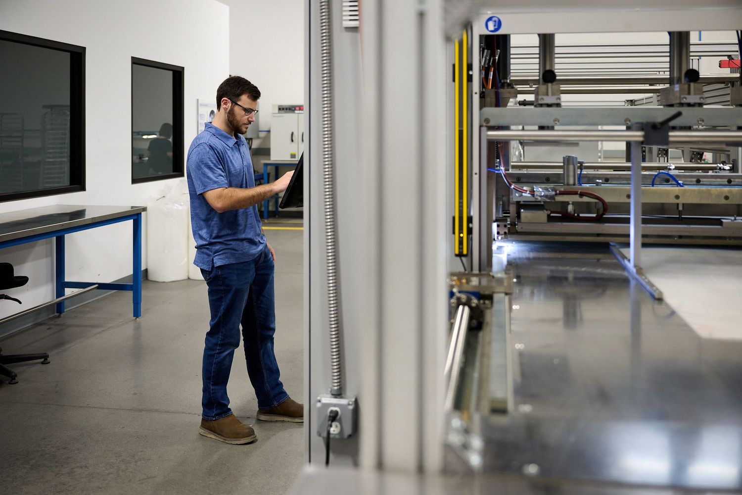 Male engineer in blue shirt using tablet to monitor automated production line in modern facility.