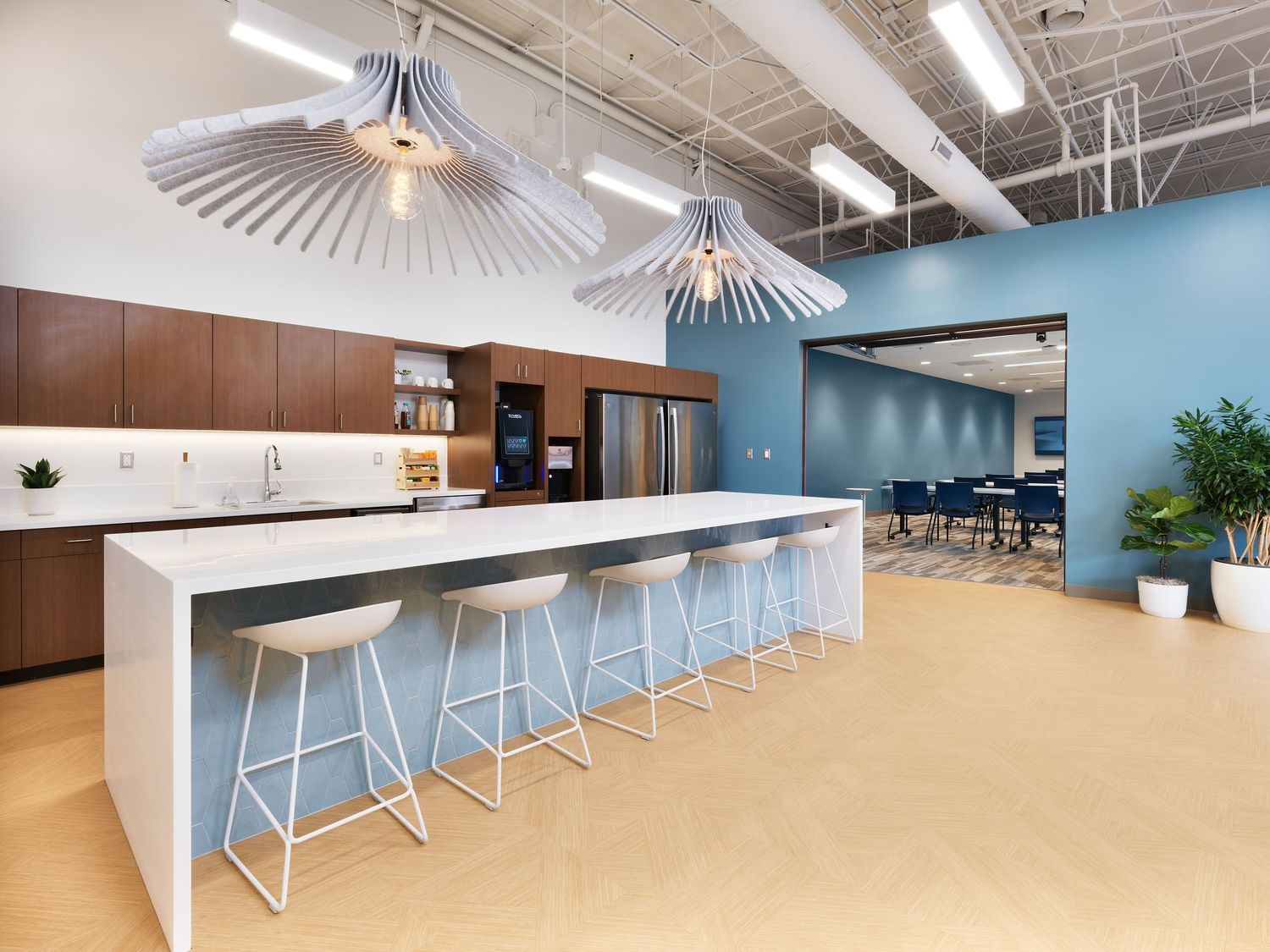 Modern office break room with a white island, bar stools, and decorative pendant lights.
