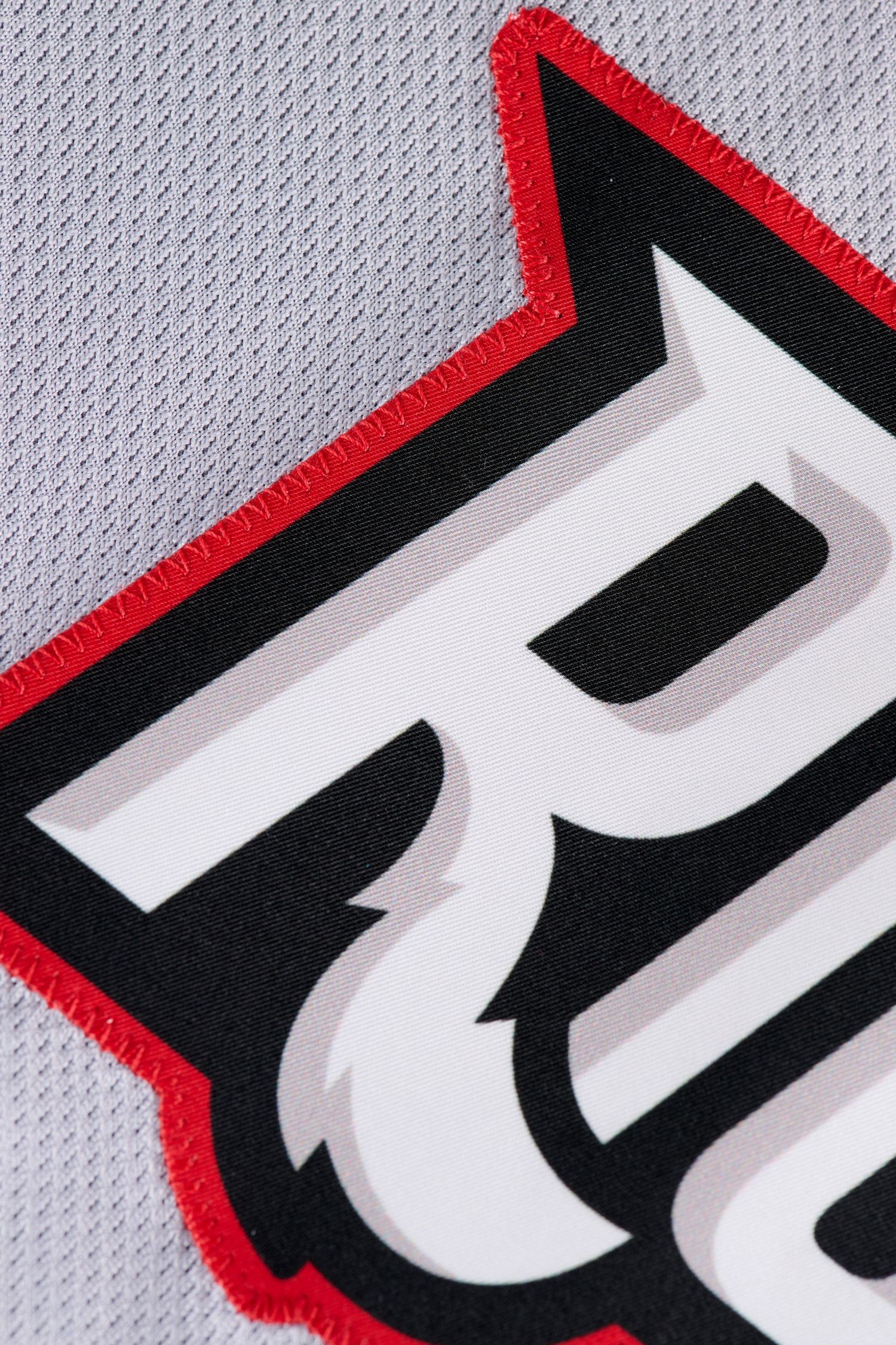 Close-up of a gray athletic jersey featuring a bold black and red letter R logo with stitched detailing.