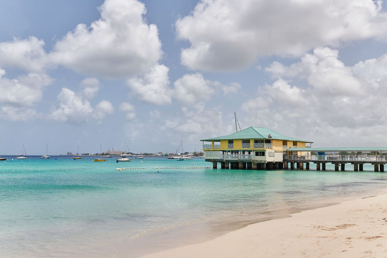 Turquoise Caribbean waters with a yellow wooden pier house on stilts under partly cloudy skies.