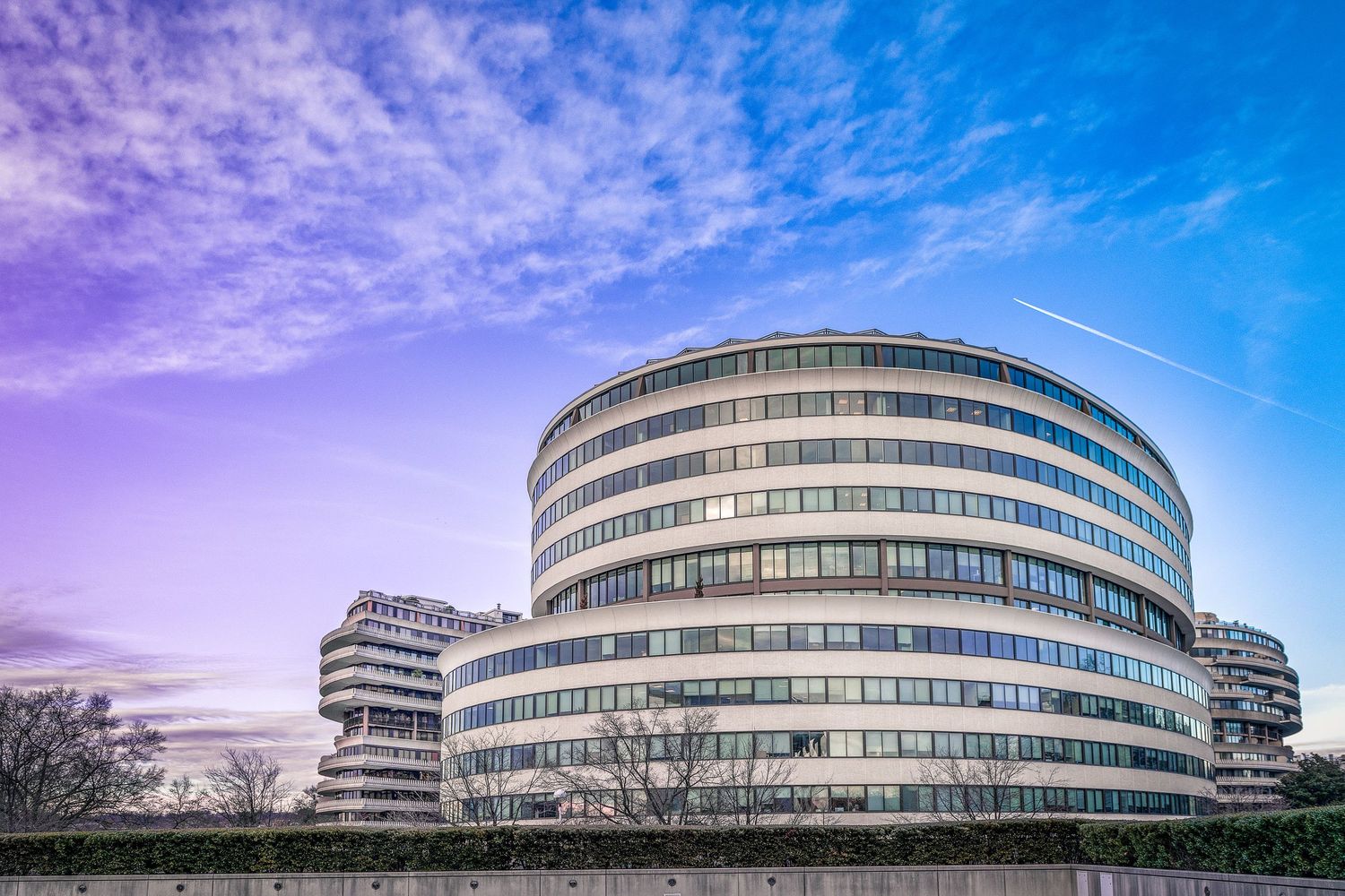 Modern circular office building with curved glass facade under a dramatic purple sky.