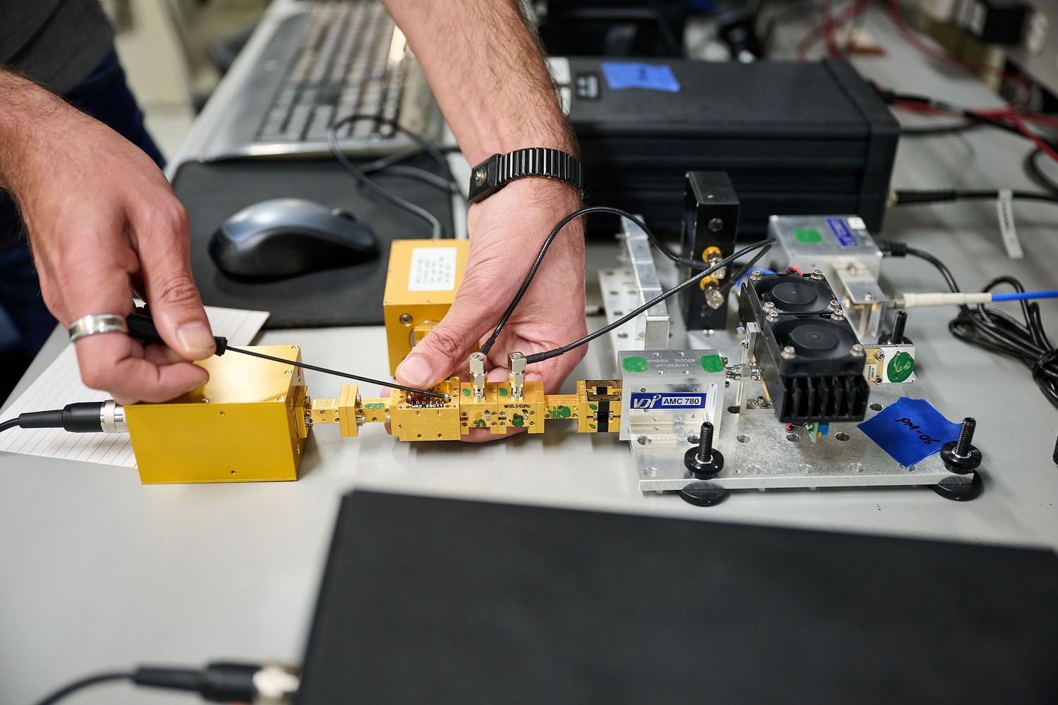 Engineer testing yellow electronic hardware components and circuit boards on laboratory workbench.