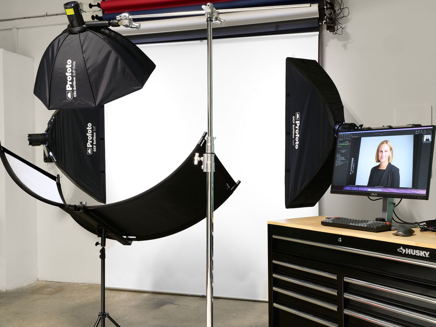 Professional photography studio setup with two softbox lights, white backdrop, and monitor displaying portrait subject.
