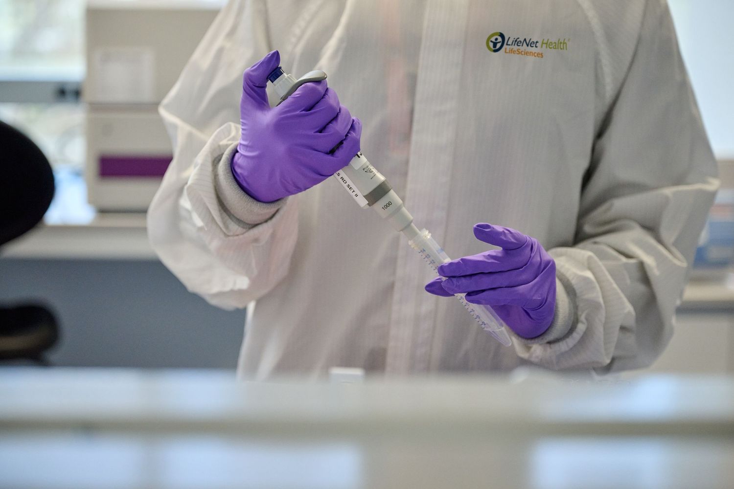 Lab technician in white coat and purple gloves filling syringe in medical laboratory.
