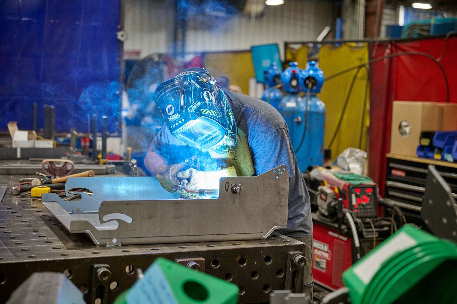 A welder in a protective helmet creates bright sparks while welding metal in a workshop.