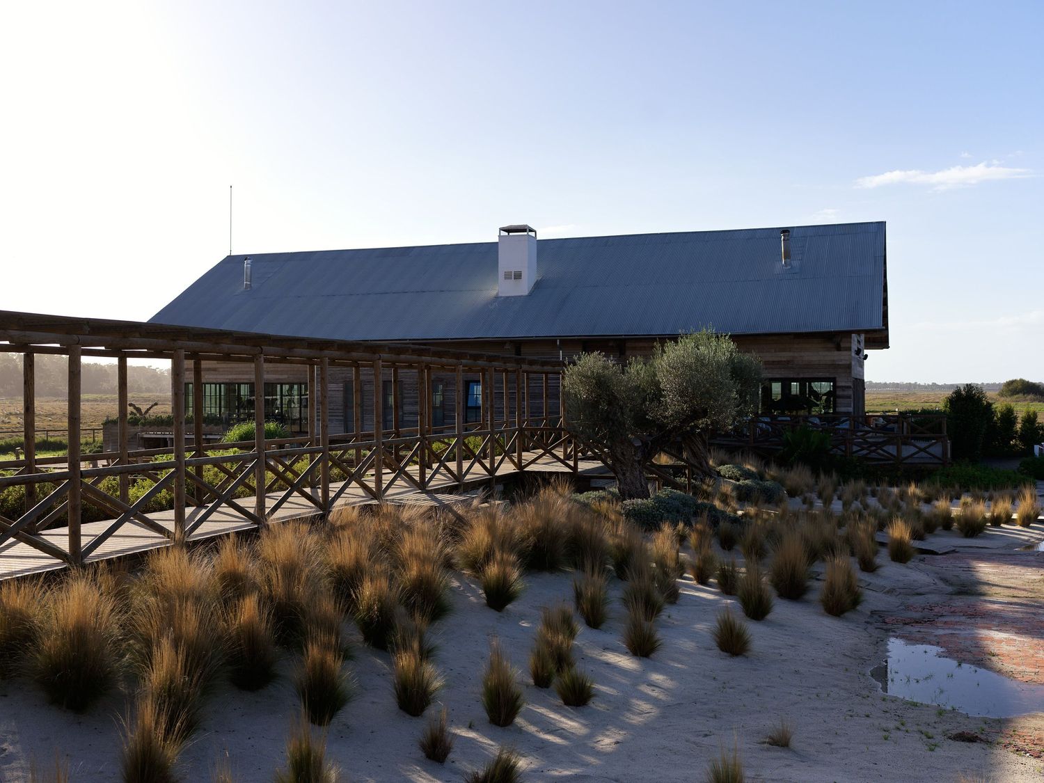 Rustic ranch-style building with wooden porch and metal roof set among dry grasslands at golden hour.