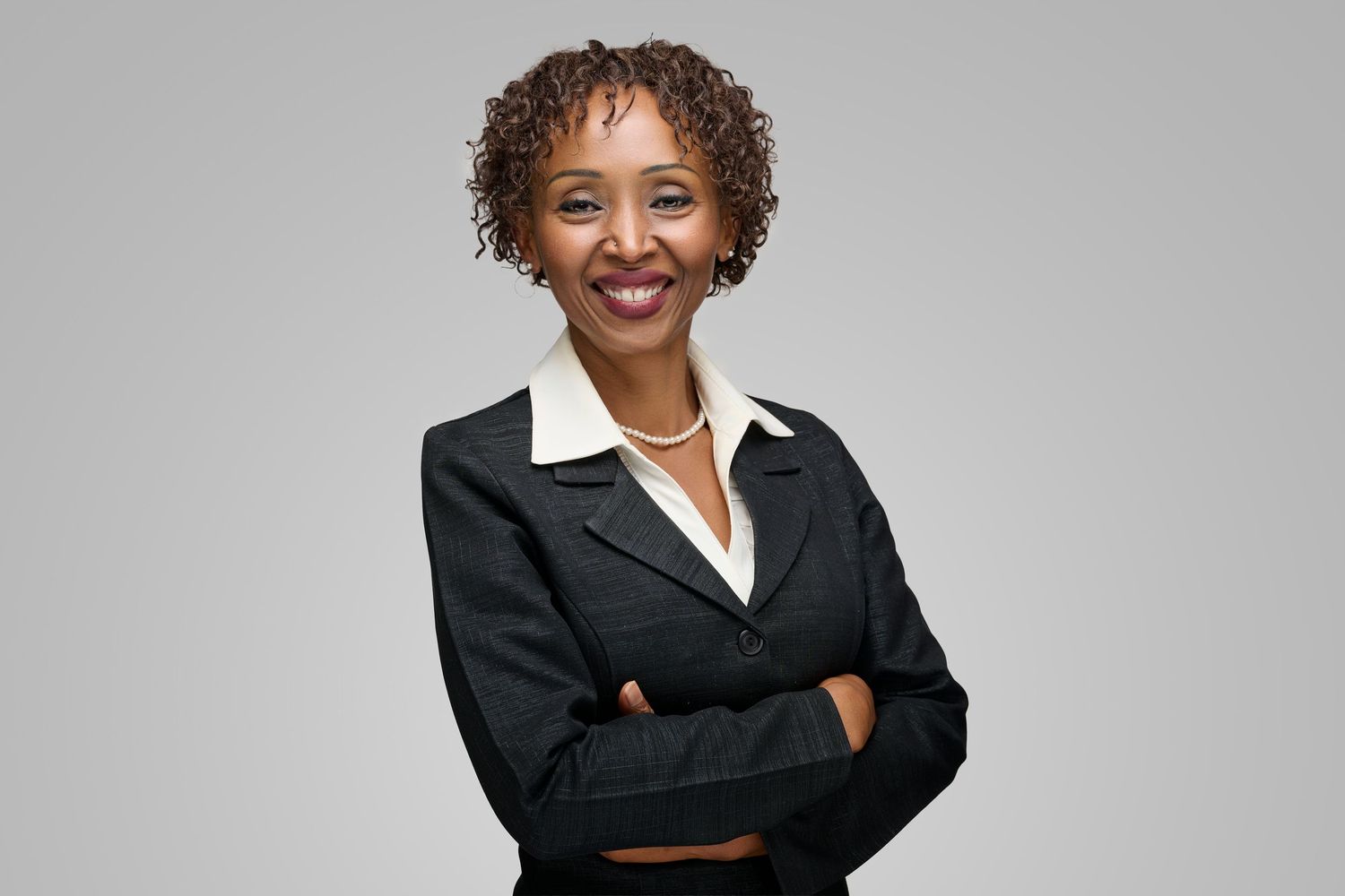 Smiling businesswoman in black suit with arms crossed against gray background.