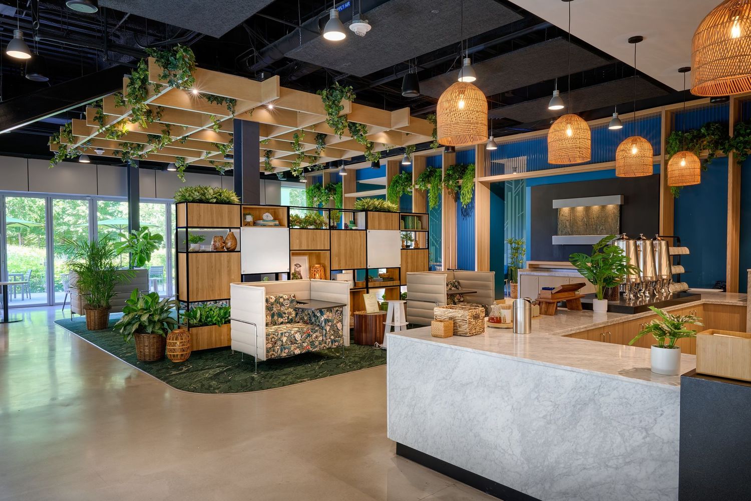 Biophilic coworking space with hanging plants, wicker pendant lights, marble counter, and lounge seating.