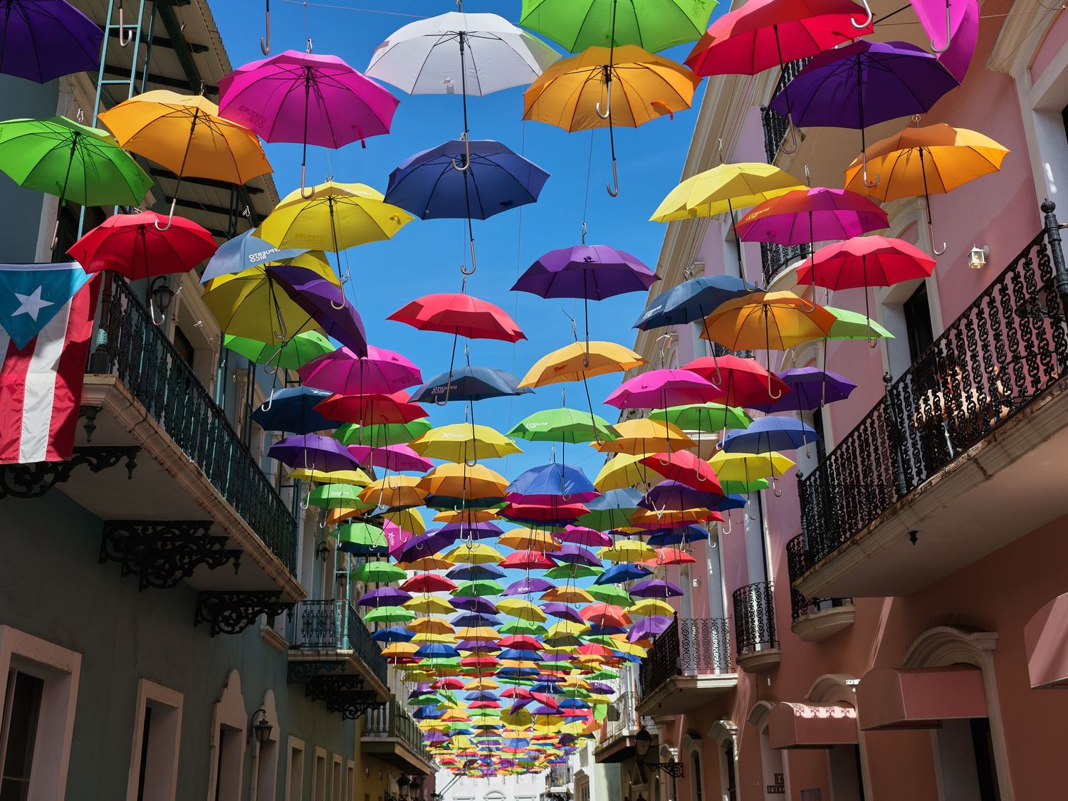 Colorful rainbow umbrellas suspended overhead along a narrow street in Old San Juan, Puerto Rico.