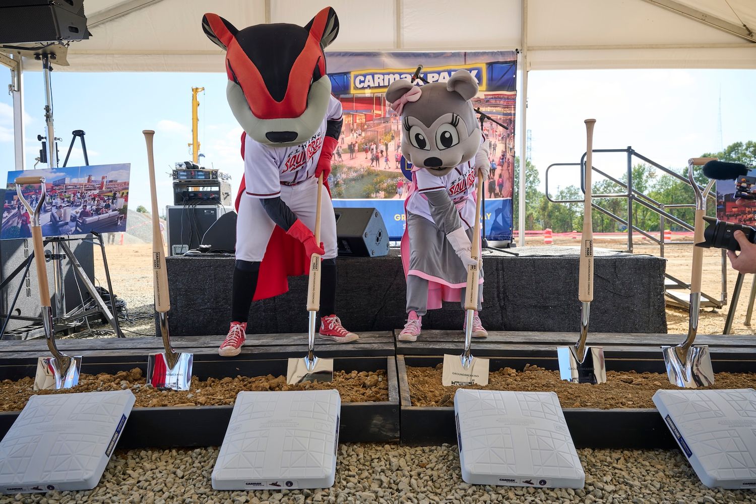 Two sports mascots in red and white uniforms participating in ceremonial groundbreaking event outdoors.