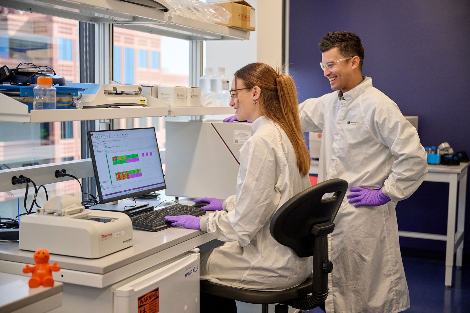 Two scientists in white lab coats working together on computer research in modern laboratory.