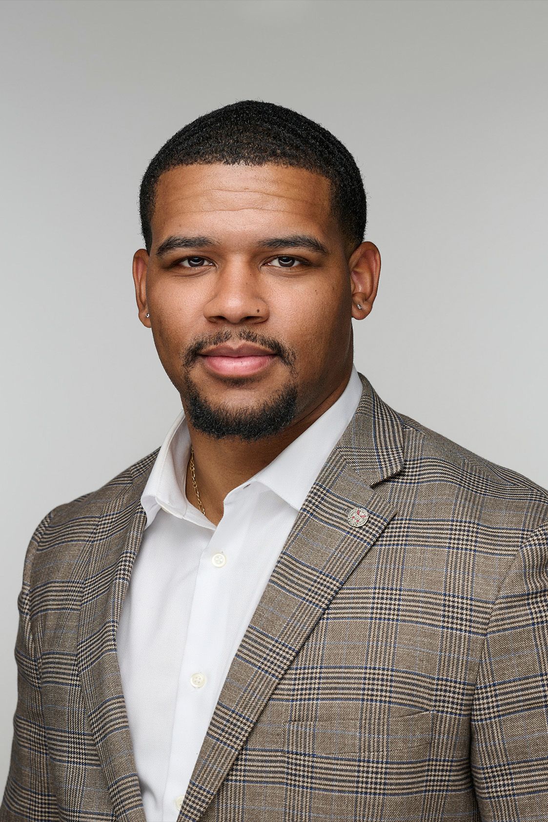 Professional headshot of a man in a plaid sport coat and white shirt on gray background.