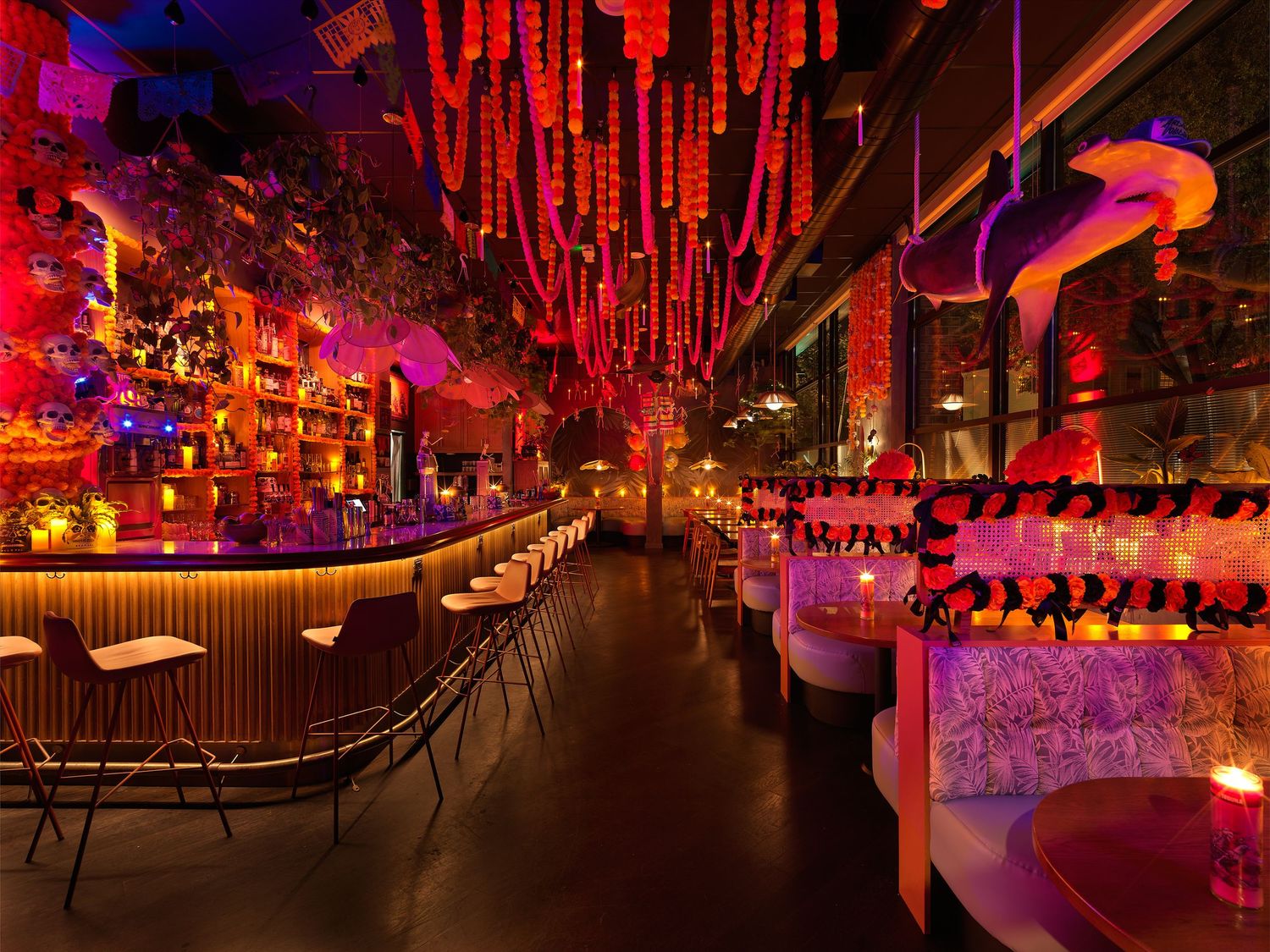 Dramatic nightclub interior with colorful hanging decor, neon lighting, and booth seating.
