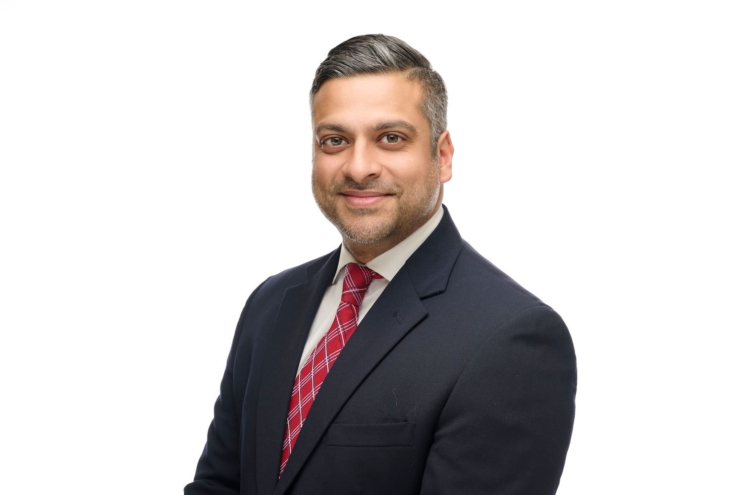 Professional headshot of a man in a navy suit with a red tie, arms crossed, on a white background.