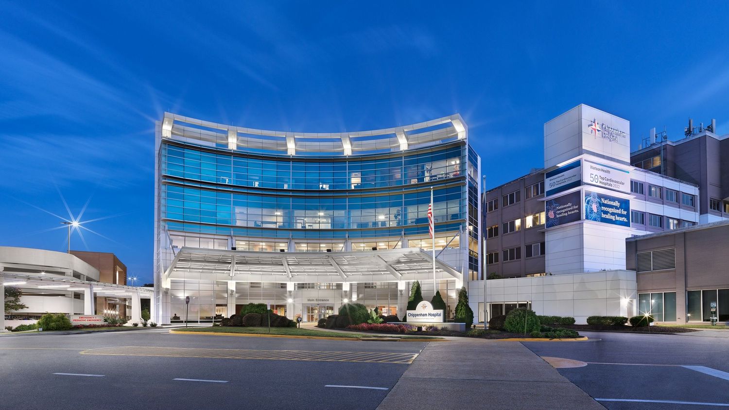 Contemporary medical center building with curved glass facade illuminated at twilight.